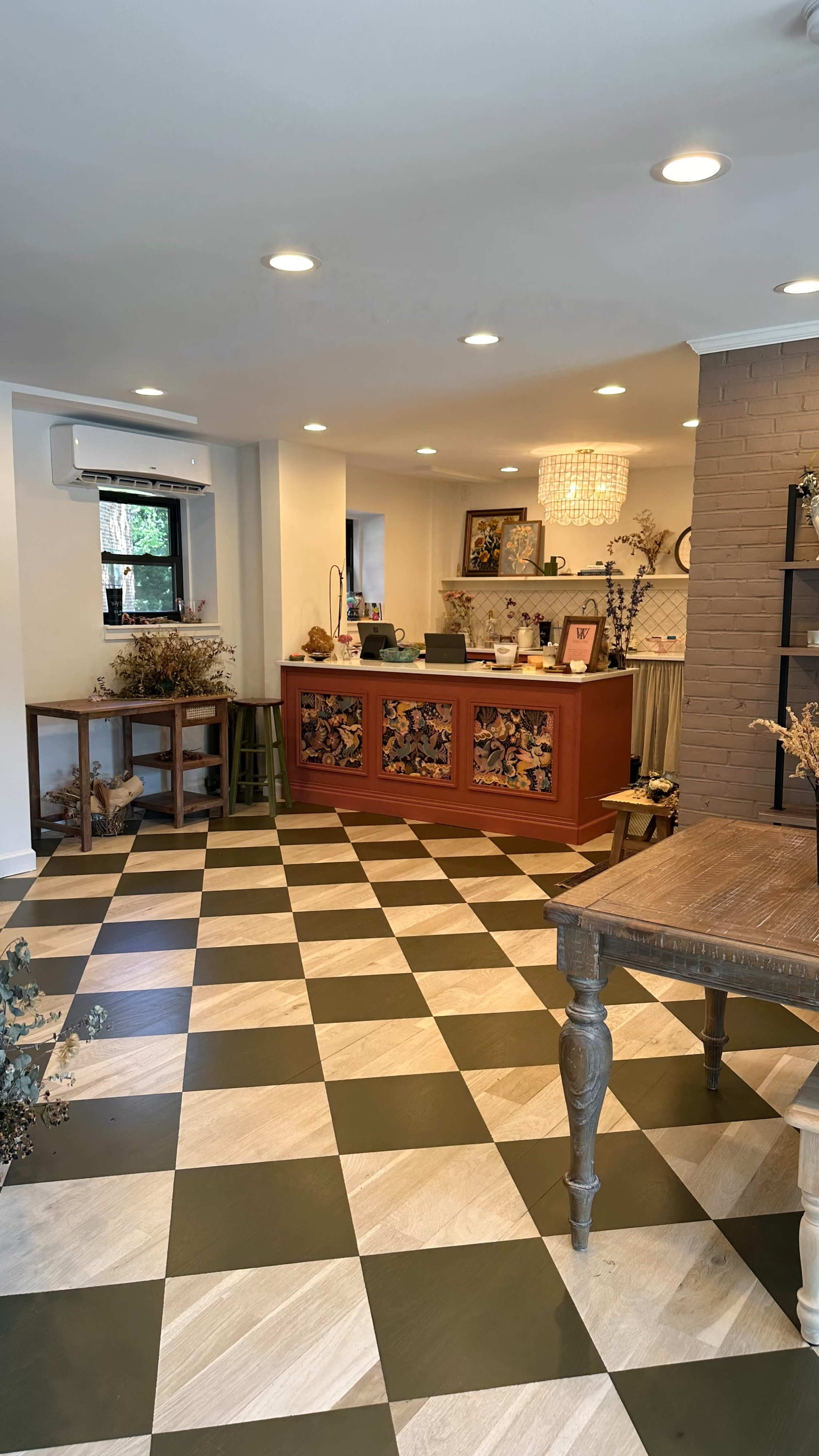 A well-lit interior space with a checkered floor, a reception desk featuring decorative panels, and various furniture and decor items arranged around the room.