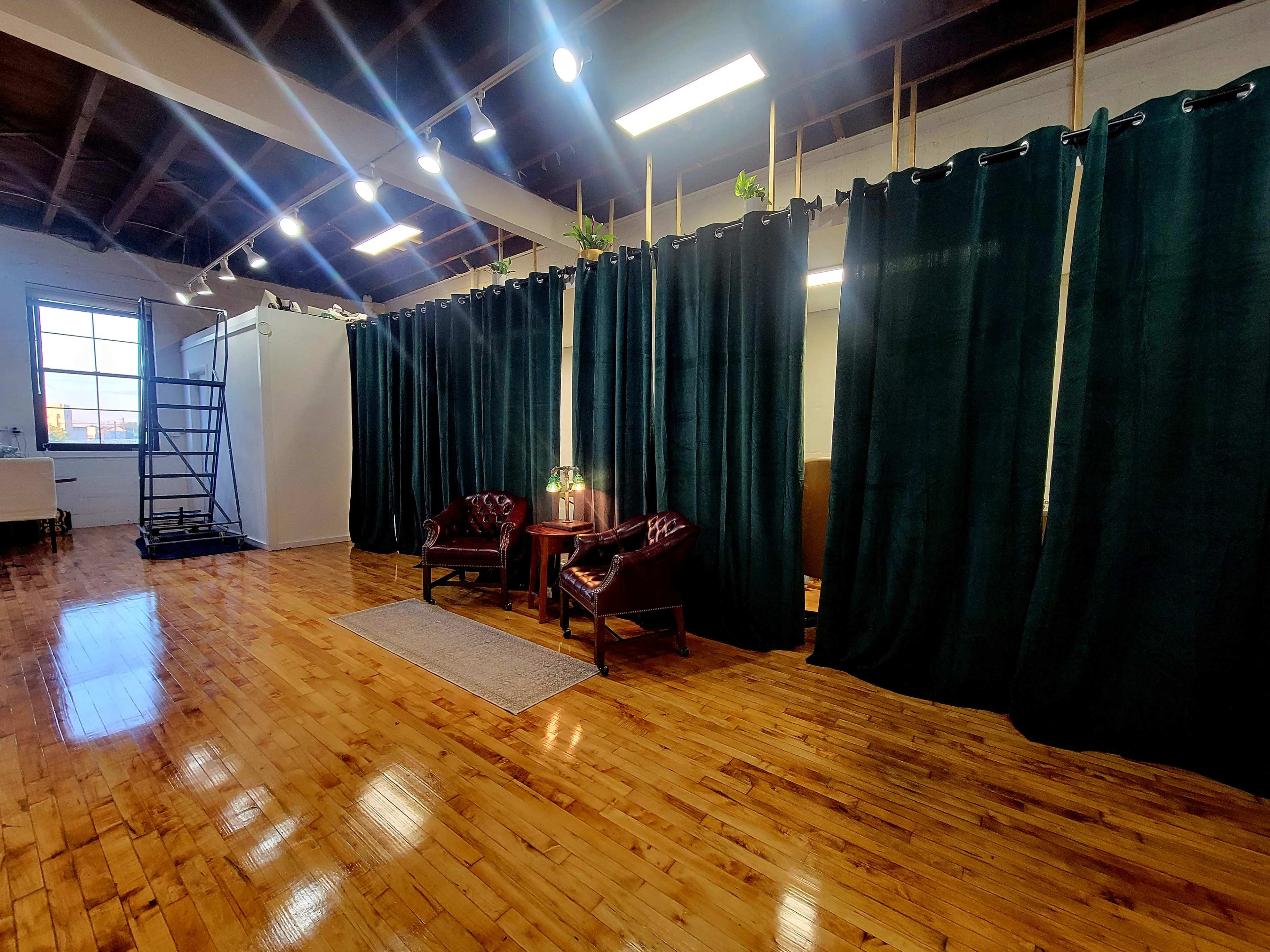The image shows a spacious interior with polished wooden floors, two leather chairs, a small side table, and dark curtains creating a partition.