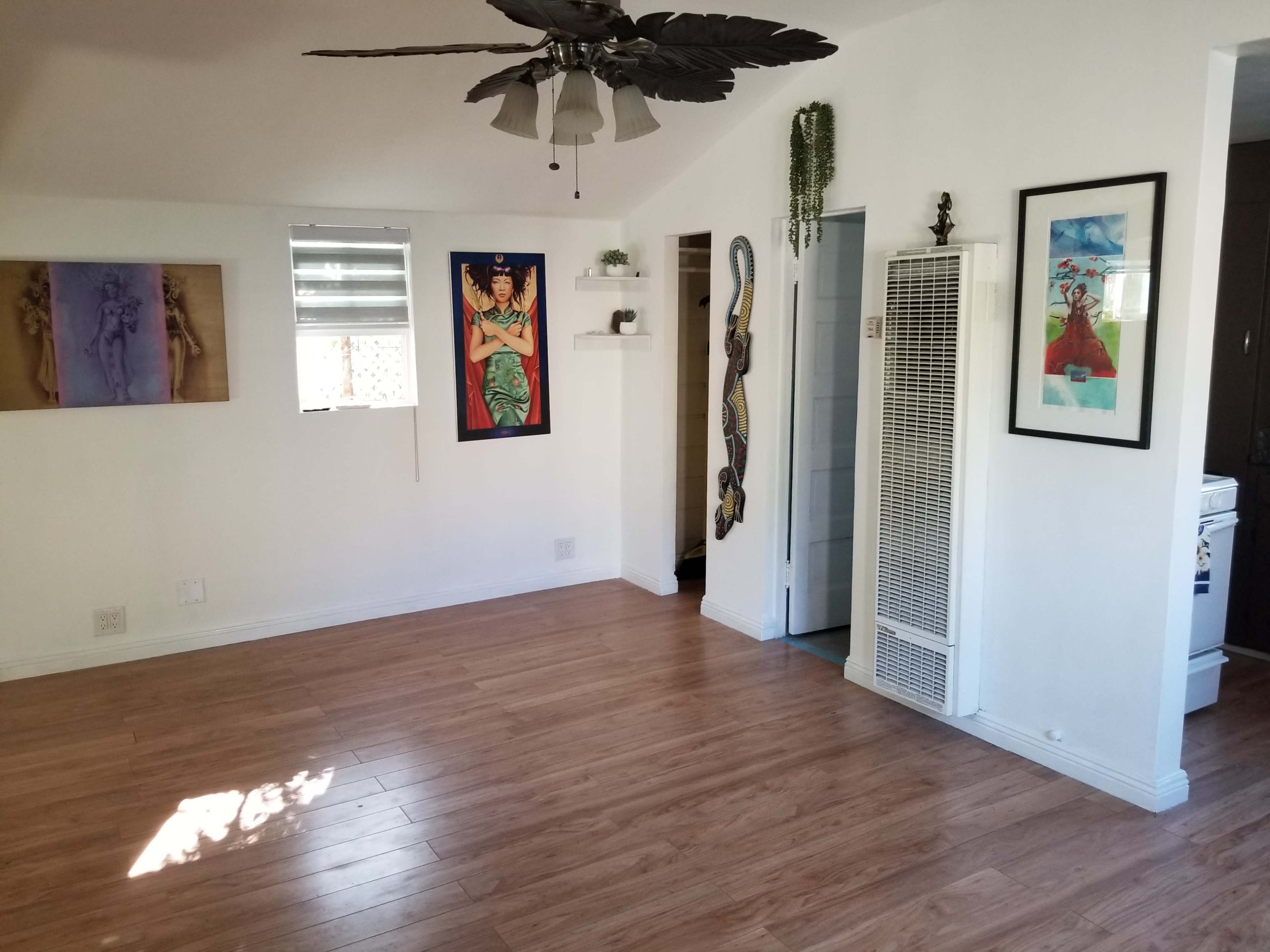 The image shows a spacious room with light hardwood flooring, wall art, and a ceiling fan.