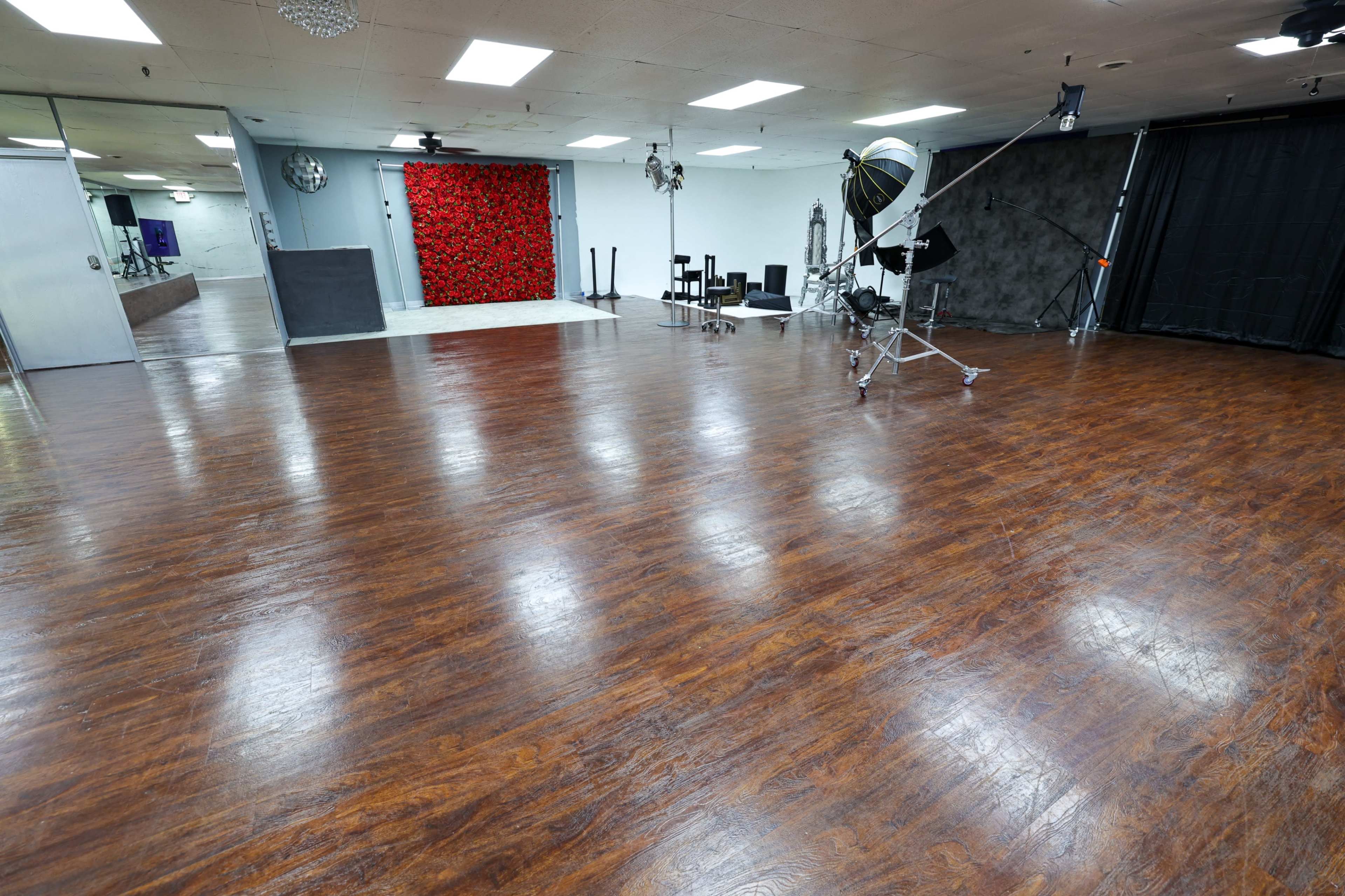 A spacious studio with a polished wooden floor, featuring a red floral backdrop and various photography equipment set up in the background.