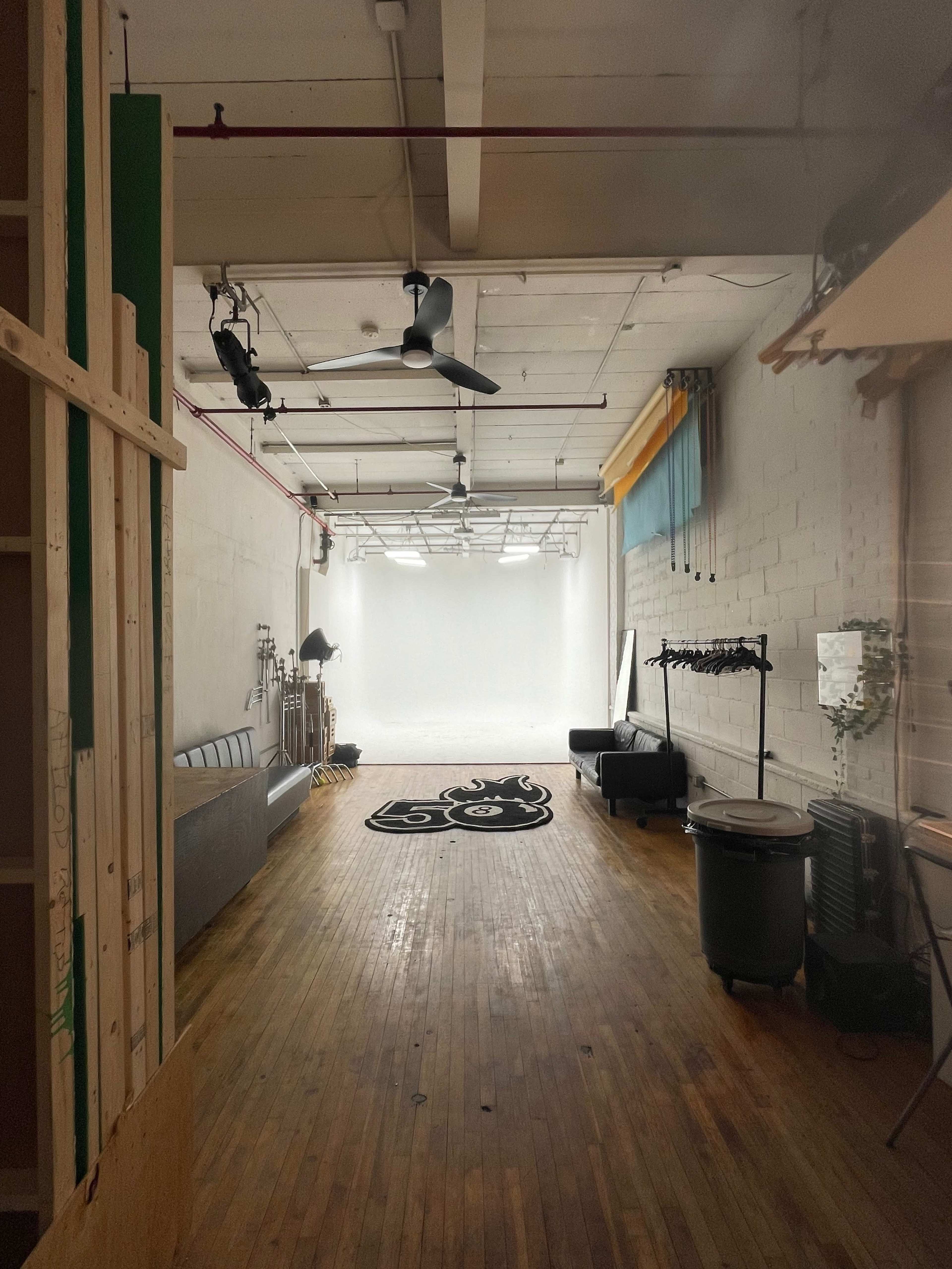 A spacious studio with wooden floors, a gray sofa, and a bright white backdrop at the far end.