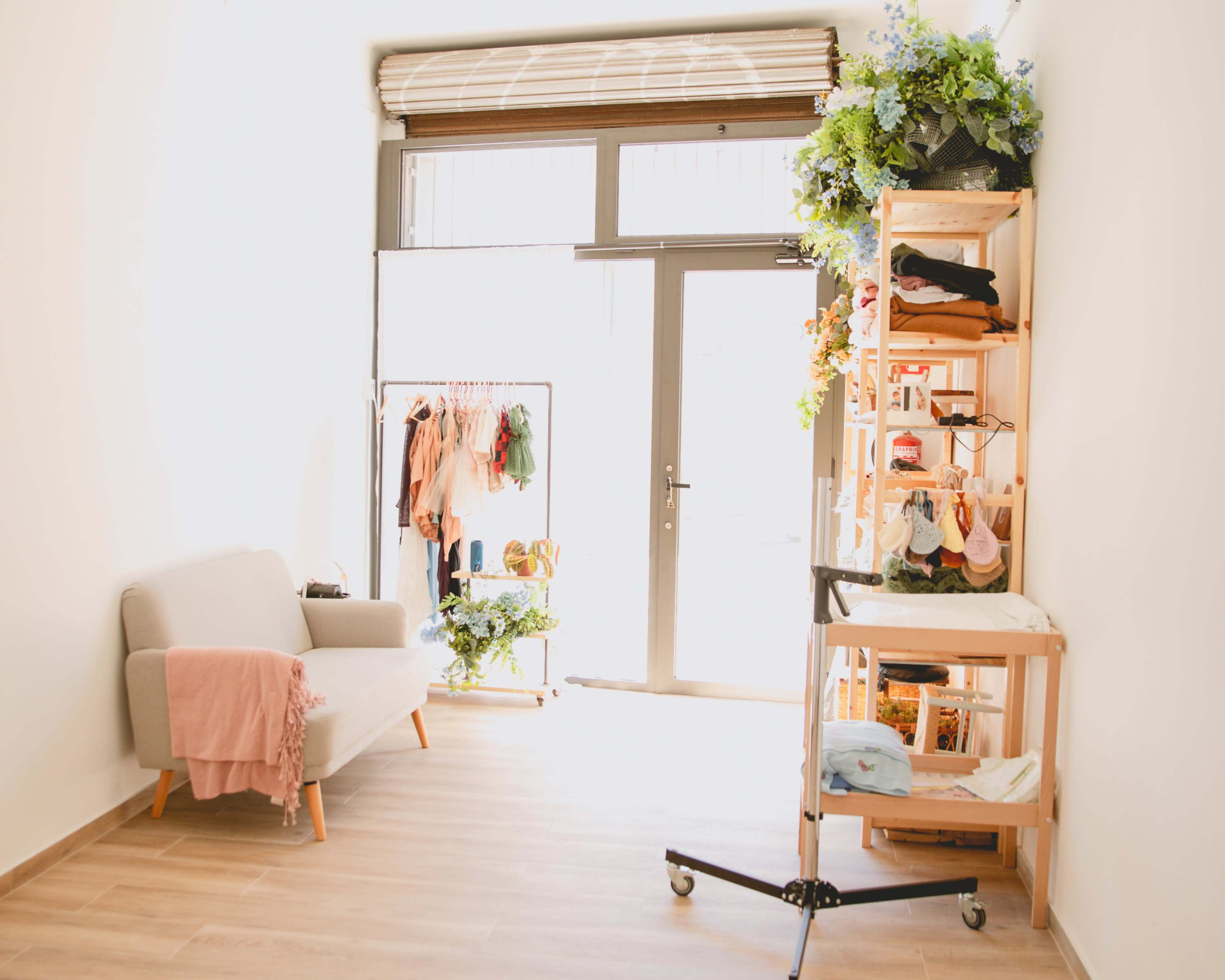 A bright, minimalistic shop interior with a seating area, clothing rack, and a display stand filled with merchandise.