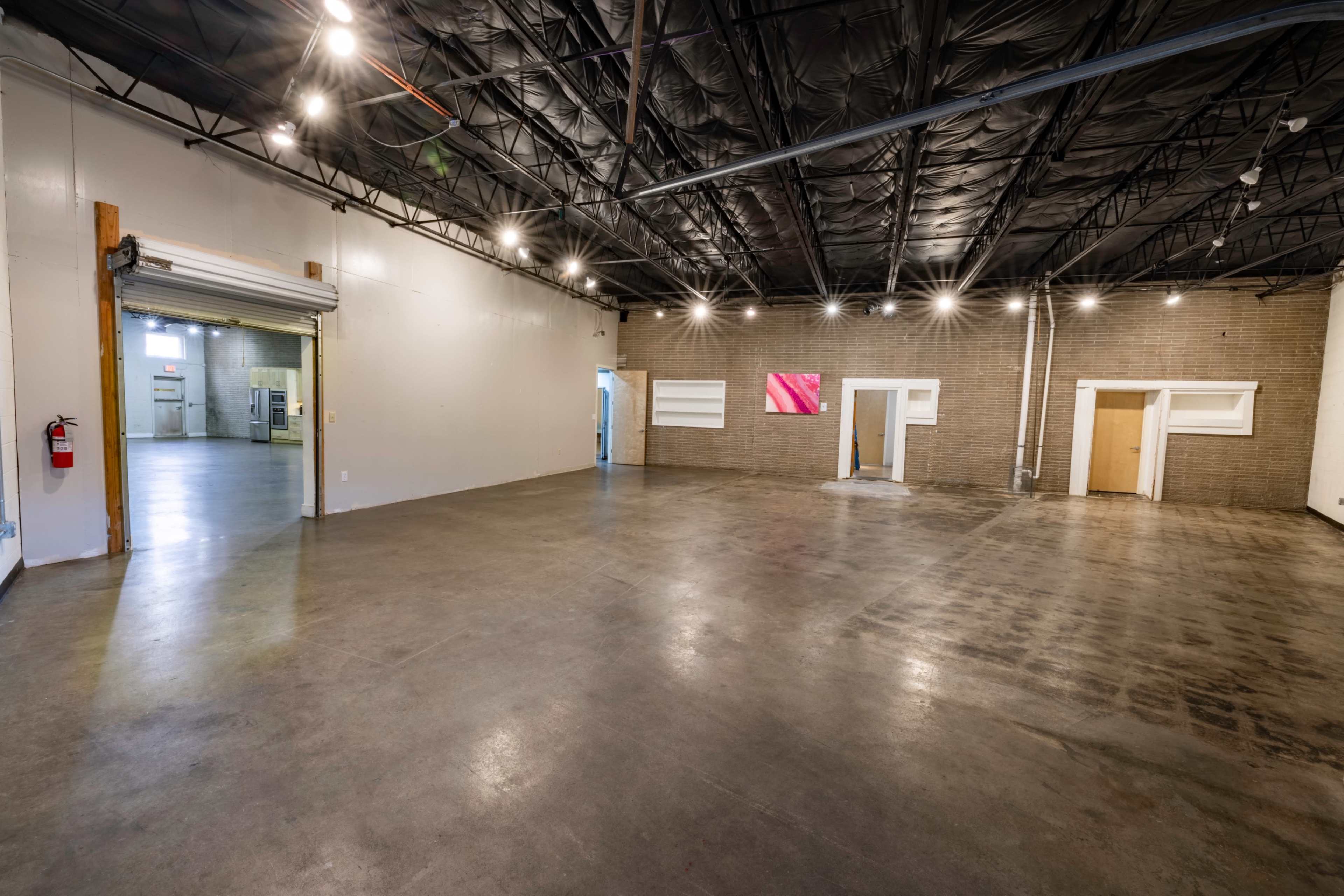 A spacious, unfinished commercial interior with concrete flooring, exposed beams, and minimal wall features.