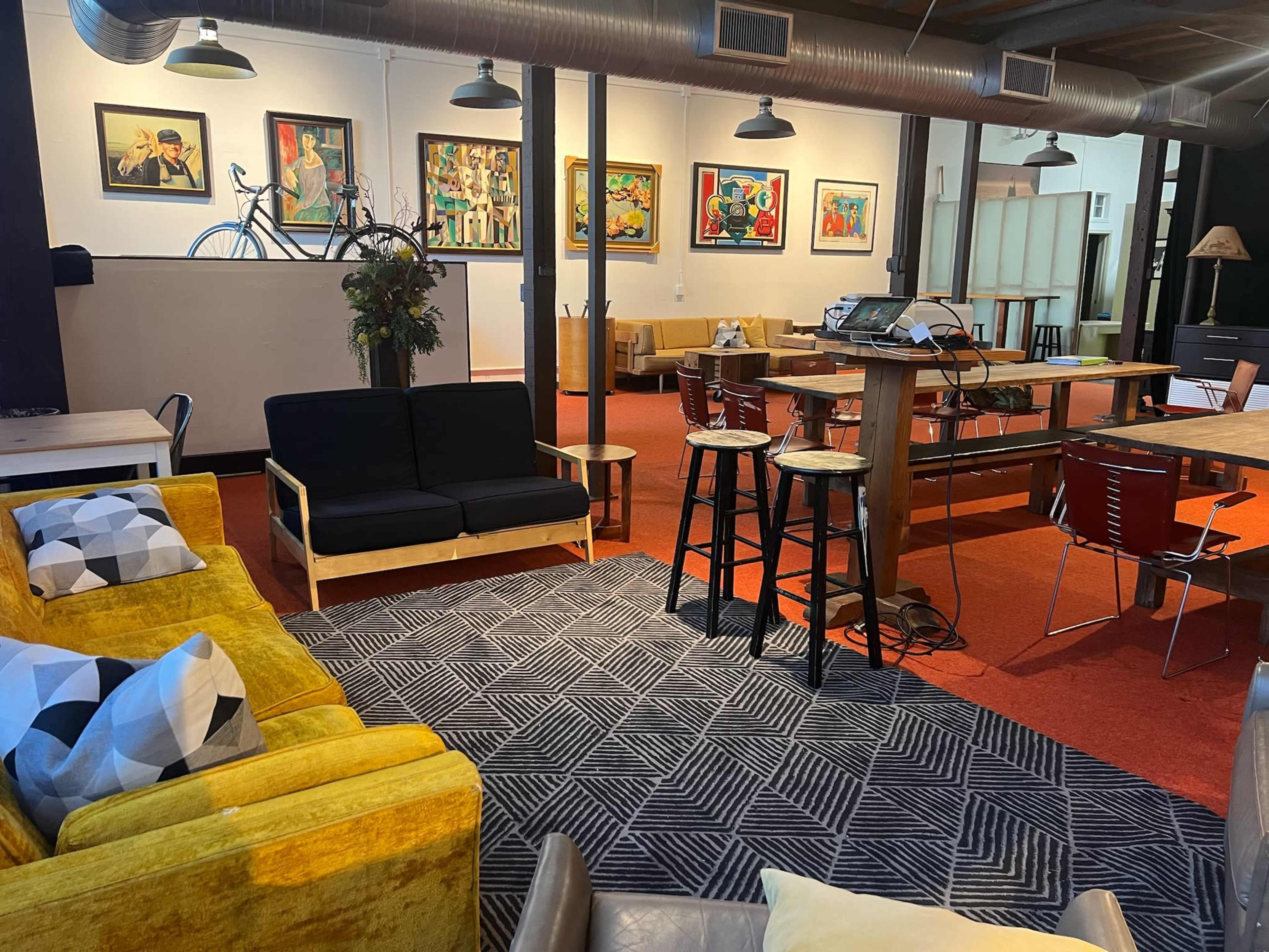 The image shows a spacious, modern interior with colorful seating, a large dining table, and artwork on the walls.