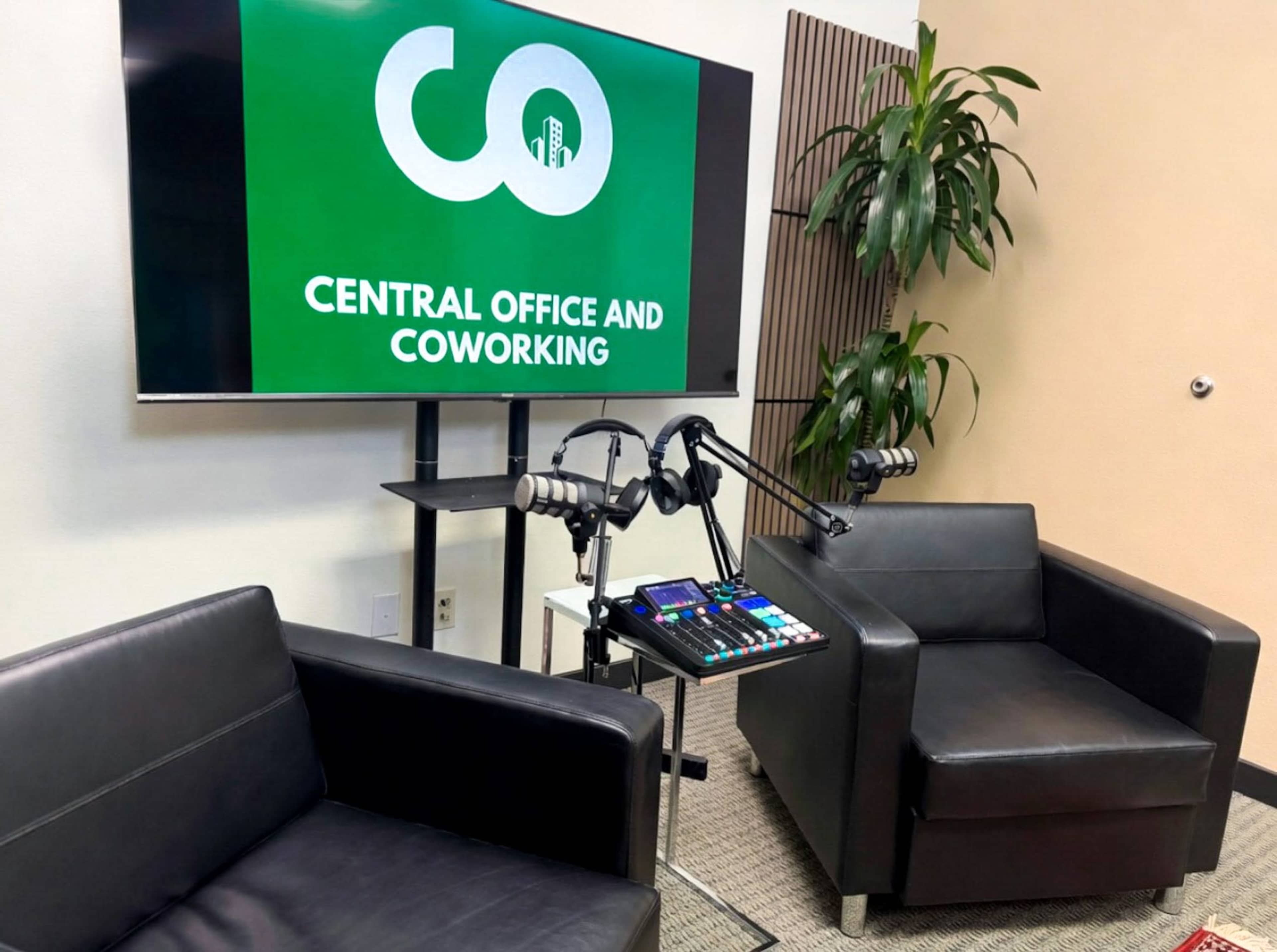 The image shows a modern workspace with two black chairs, a television displaying "CO Central Office and Coworking," and audio equipment on a small table.