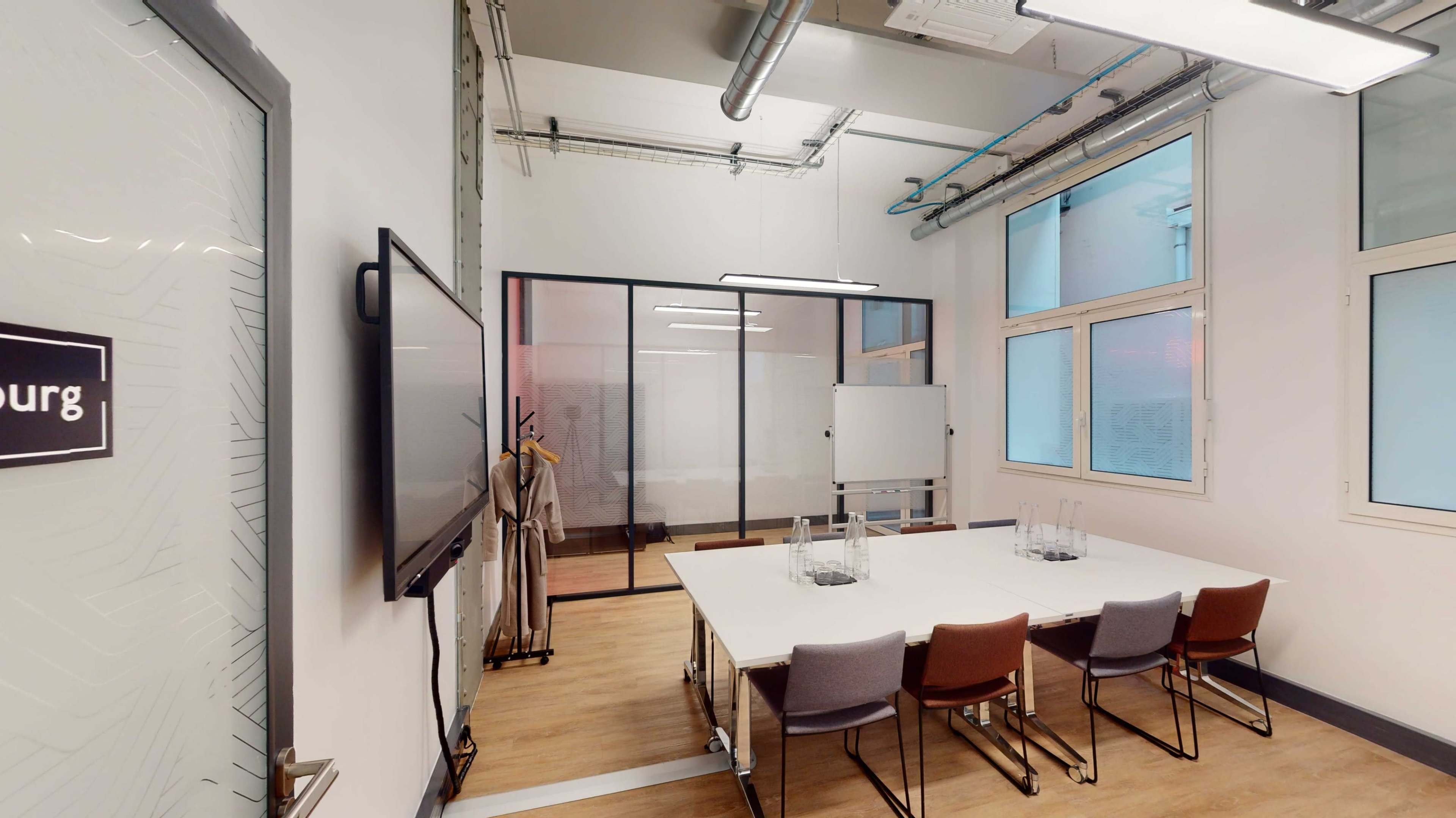 A modern conference room with a large table, six chairs, a screen, and a glass partition separating it from another workspace.