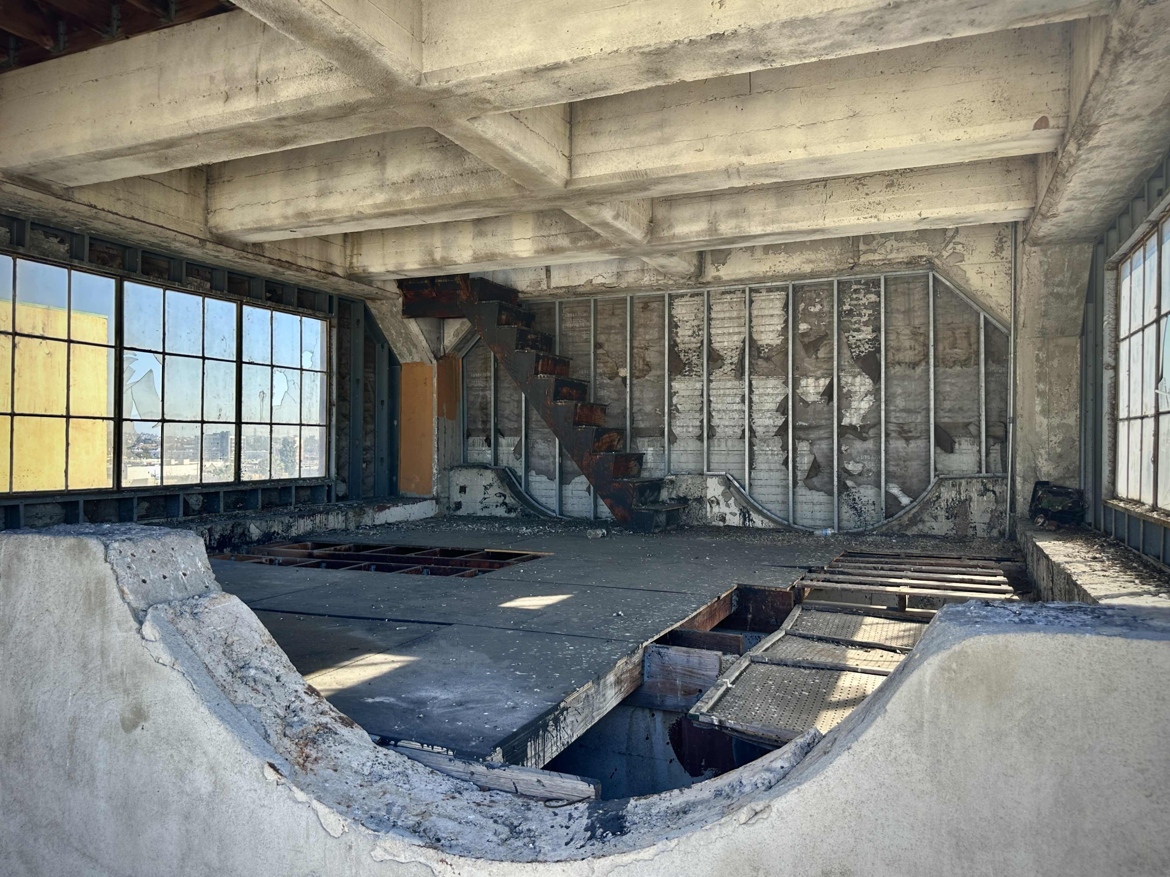 The interior of a partially constructed building features exposed concrete walls, a staircase, and large windows with views of the outside.