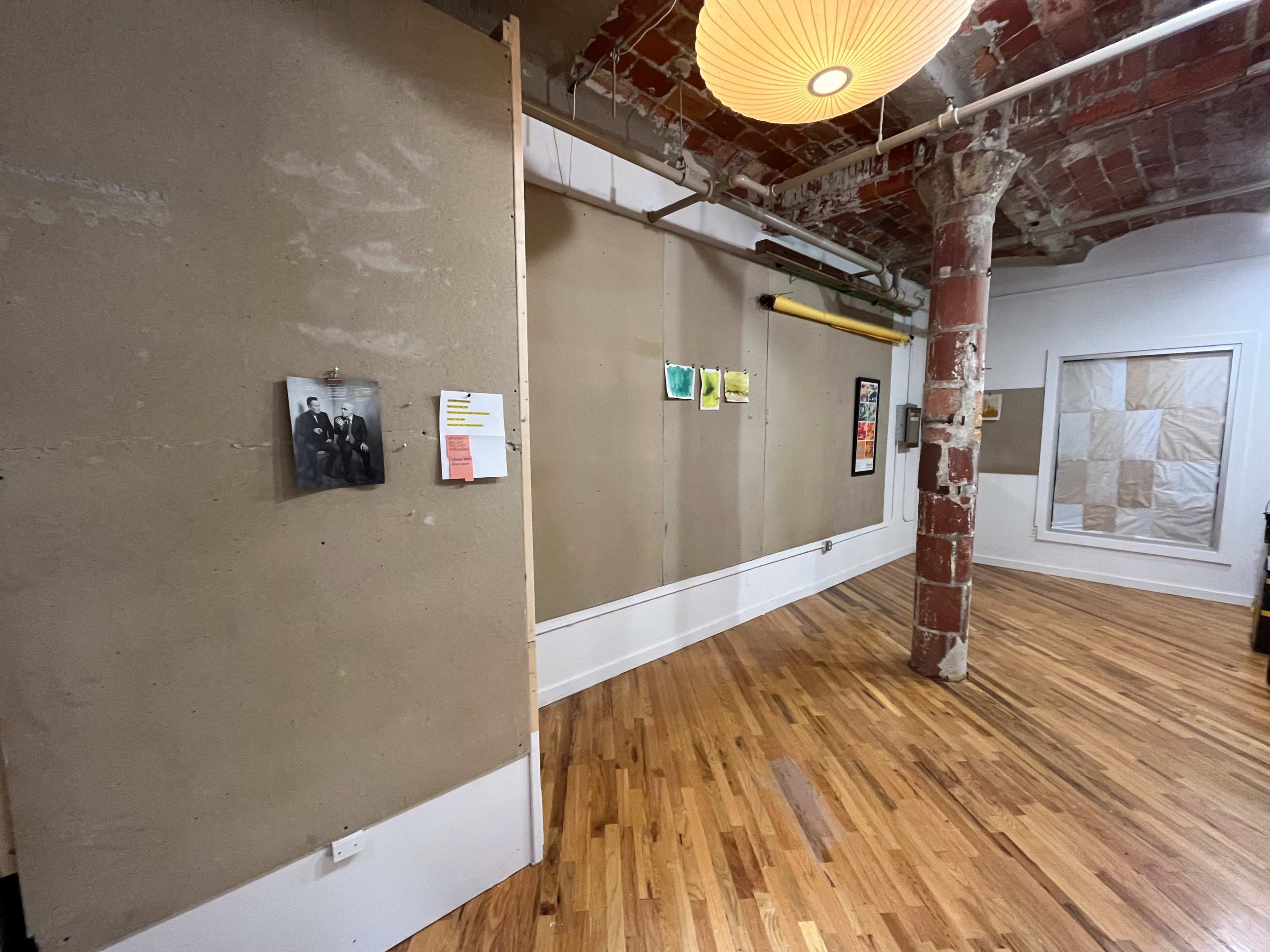 A minimalist interior space with bare walls, wooden flooring, and a mix of artwork and photographs displayed.