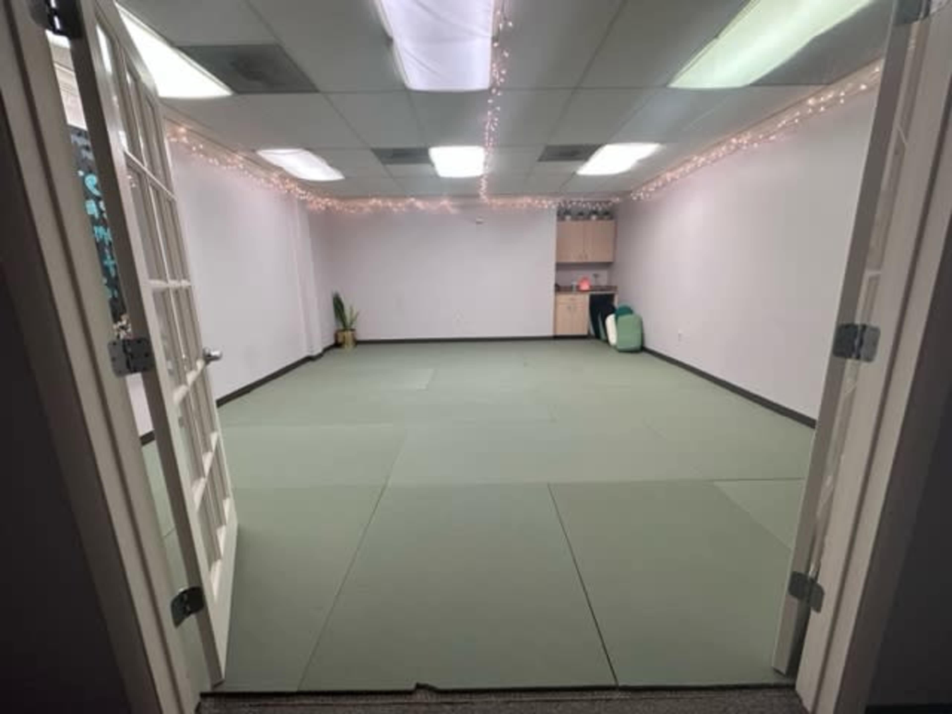 An empty room with green mats on the floor, white walls, and decorative string lights along the ceiling.