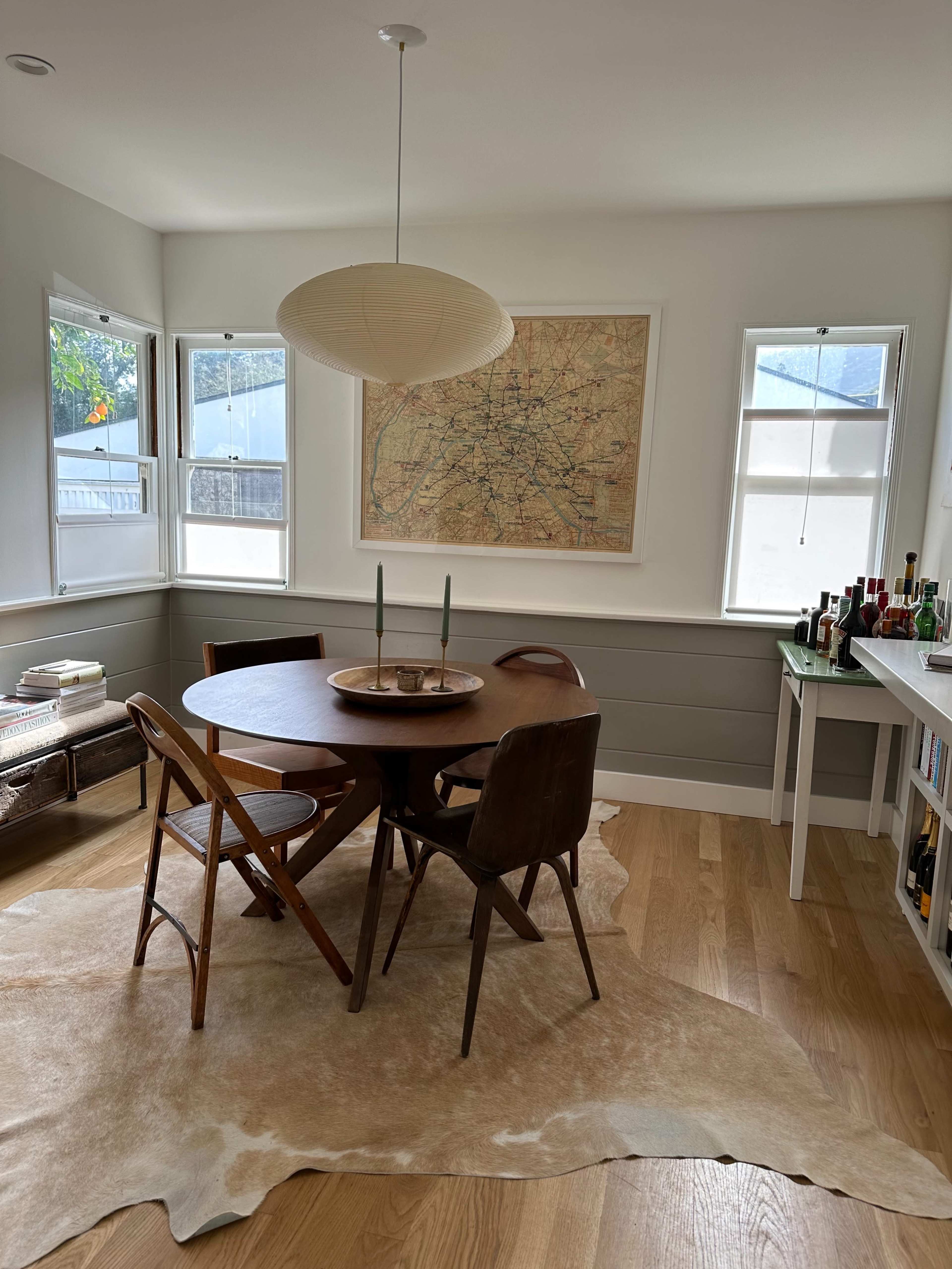 A dining area features a round wooden table surrounded by four chairs, with a large map framed on the wall and a cowhide rug on the floor.