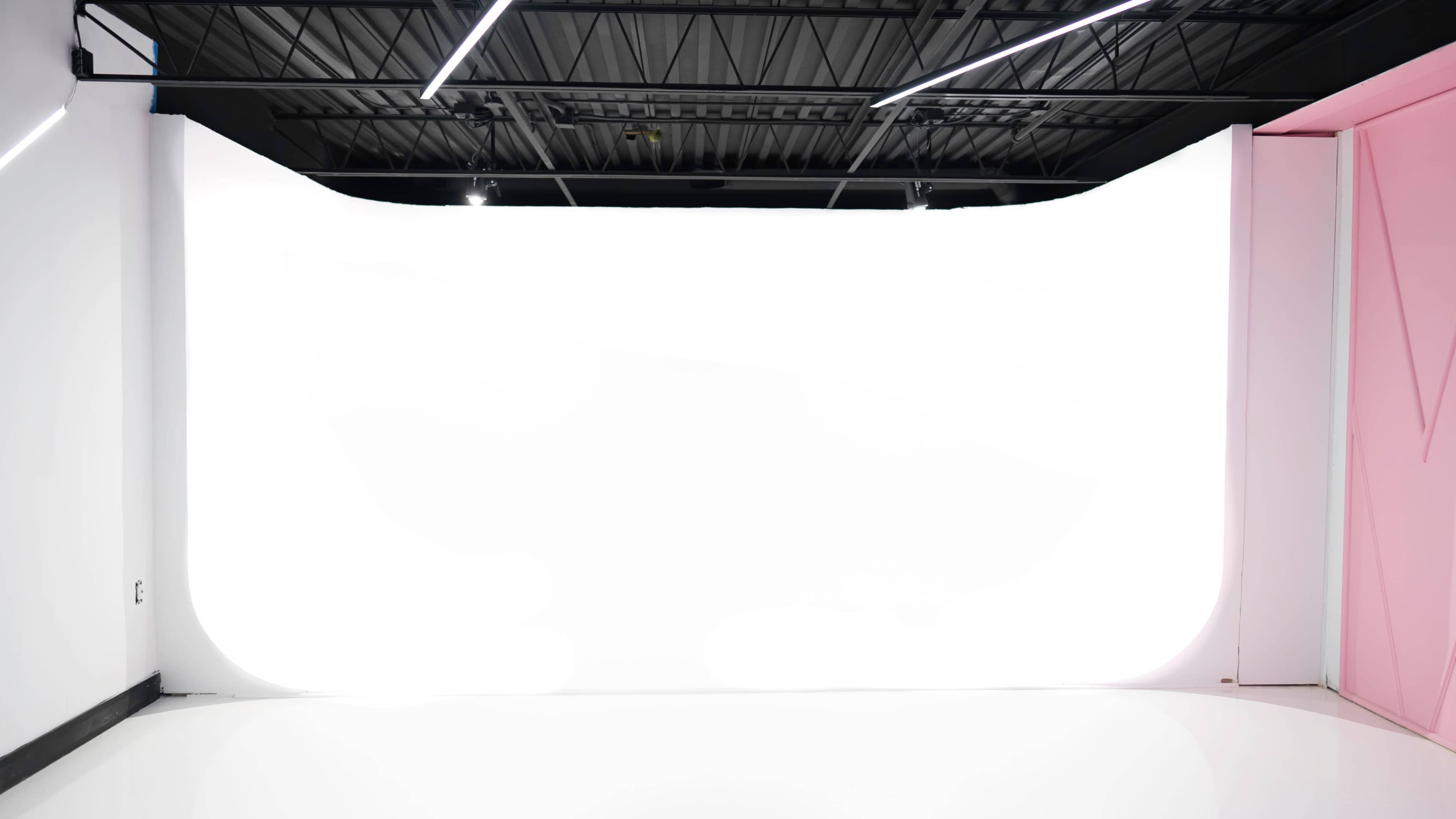 A spacious, empty studio with a large white backdrop and modern lighting fixtures.