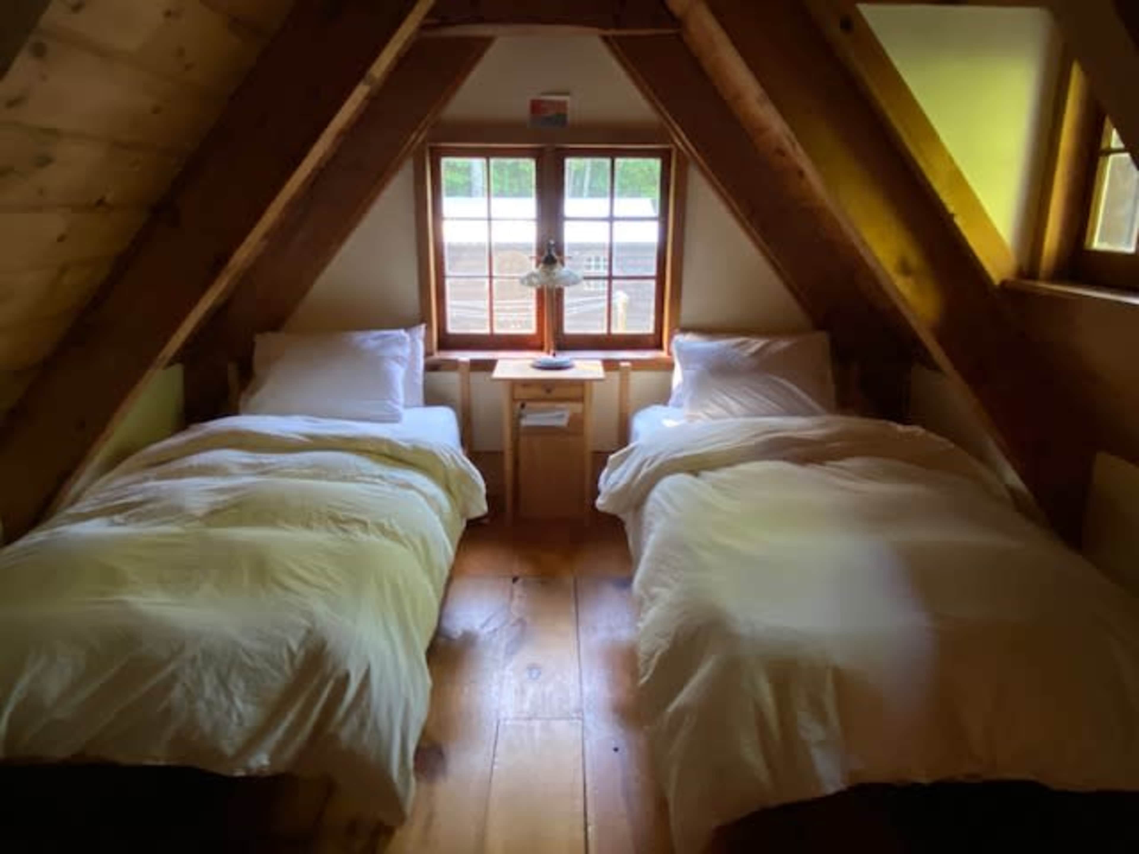 A cozy attic bedroom with two twin beds positioned next to a window, surrounded by wooden beams.