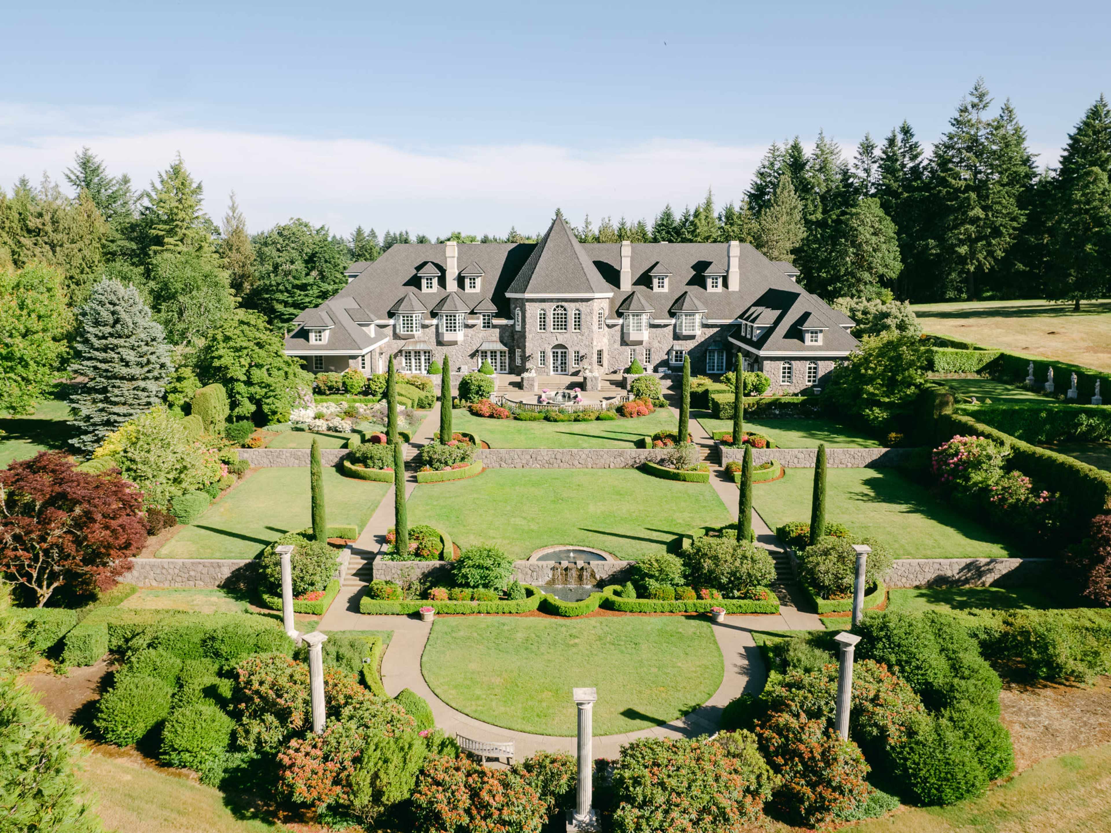 A large mansion surrounded by meticulously landscaped gardens and trees is visible in the image.