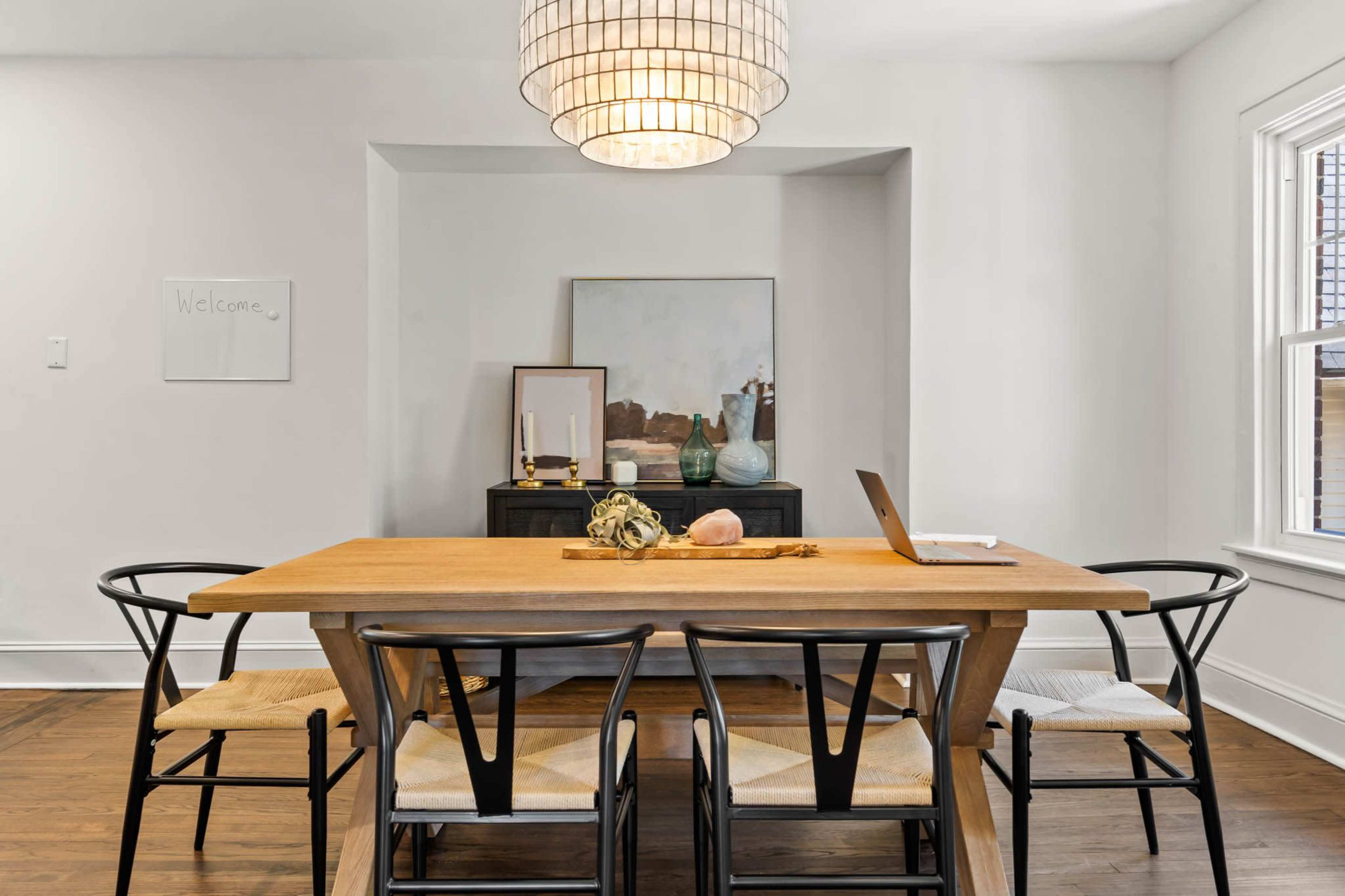 A dining room features a wooden table surrounded by black chairs, with a large pendant light overhead and decorative items on a sideboard.