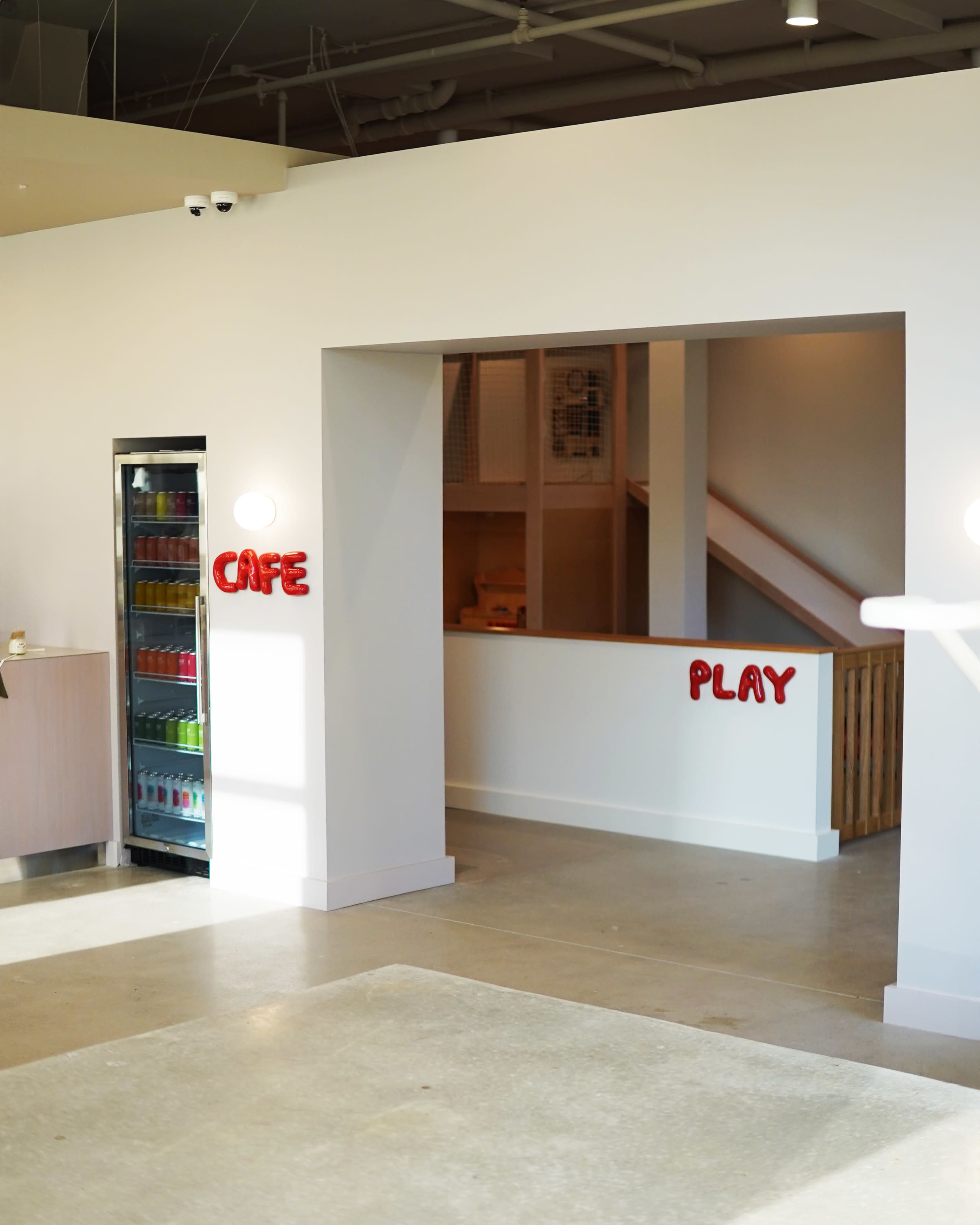 The image shows a bright interior space with a "Café" area on the left and a "Play" area beyond an open entrance on the right.