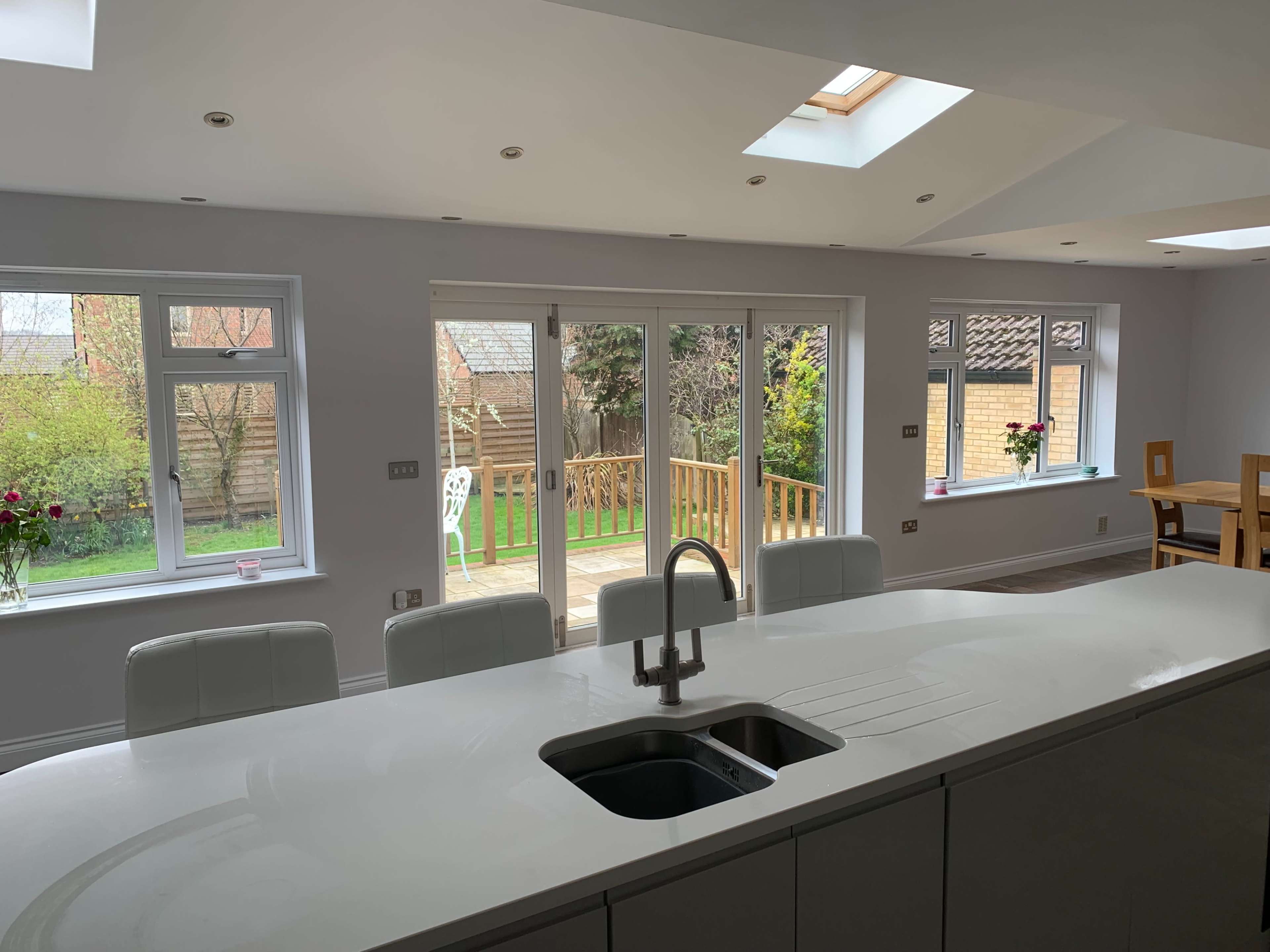 The image depicts a modern kitchen area with a large white island and open views of a backyard through glass sliding doors.