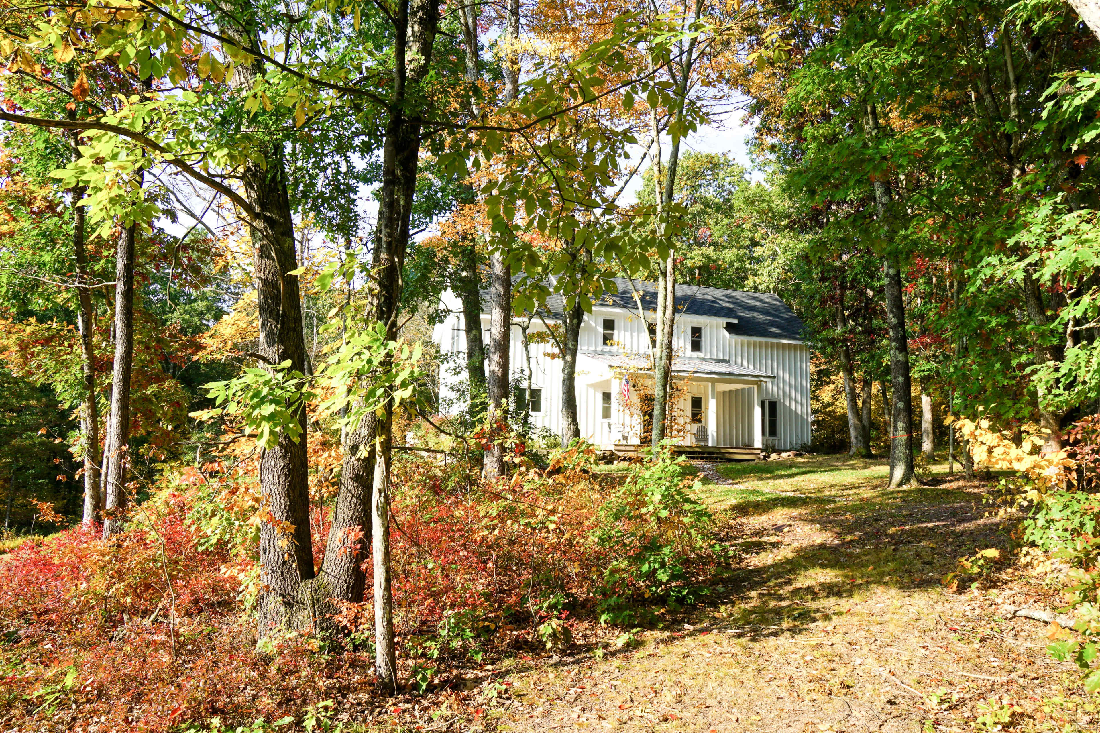 A modern two-story house is nestled among trees with colorful autumn foliage.