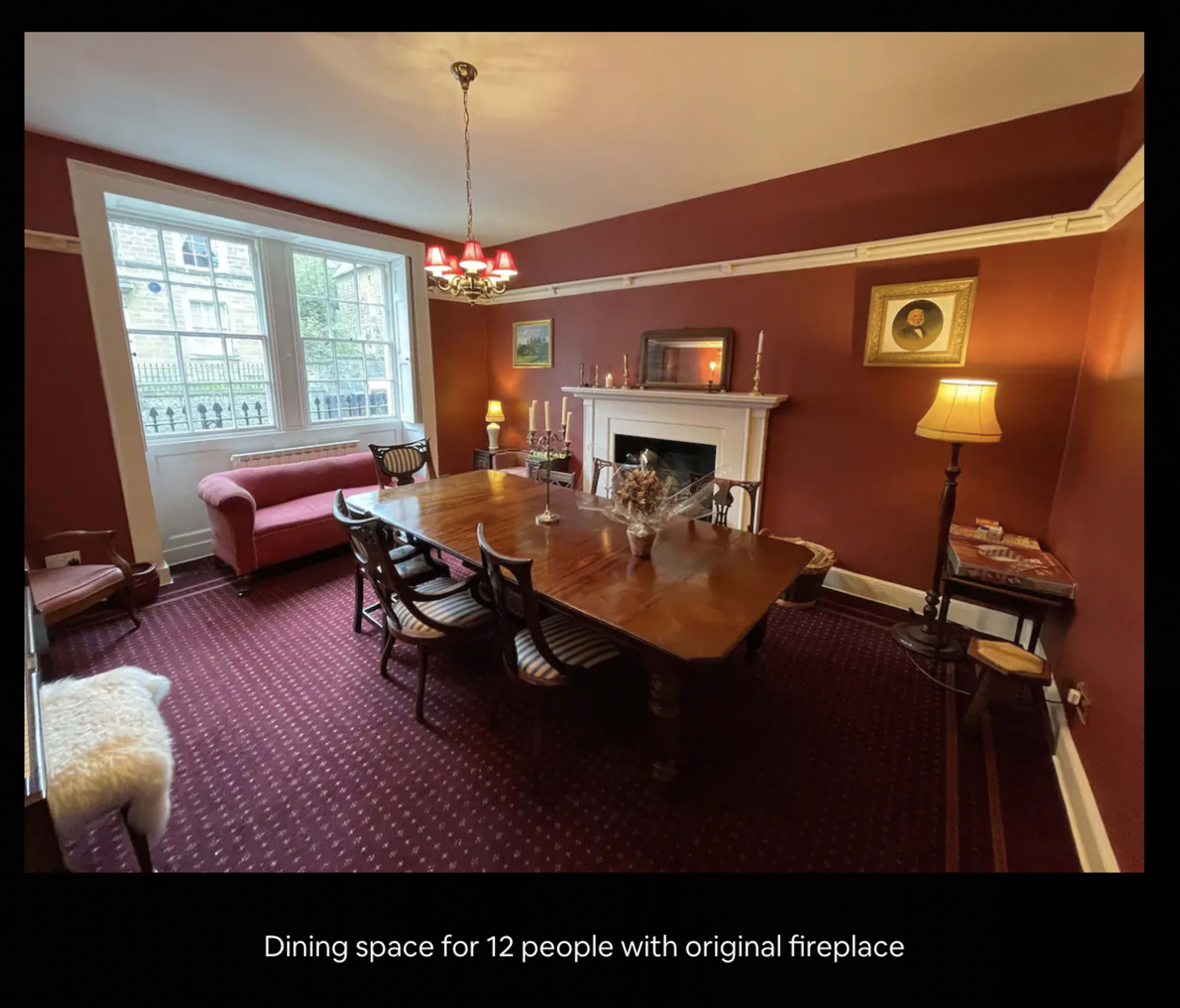 A dining room featuring a wooden table set for twelve, an original fireplace, and a mix of lighting fixtures.