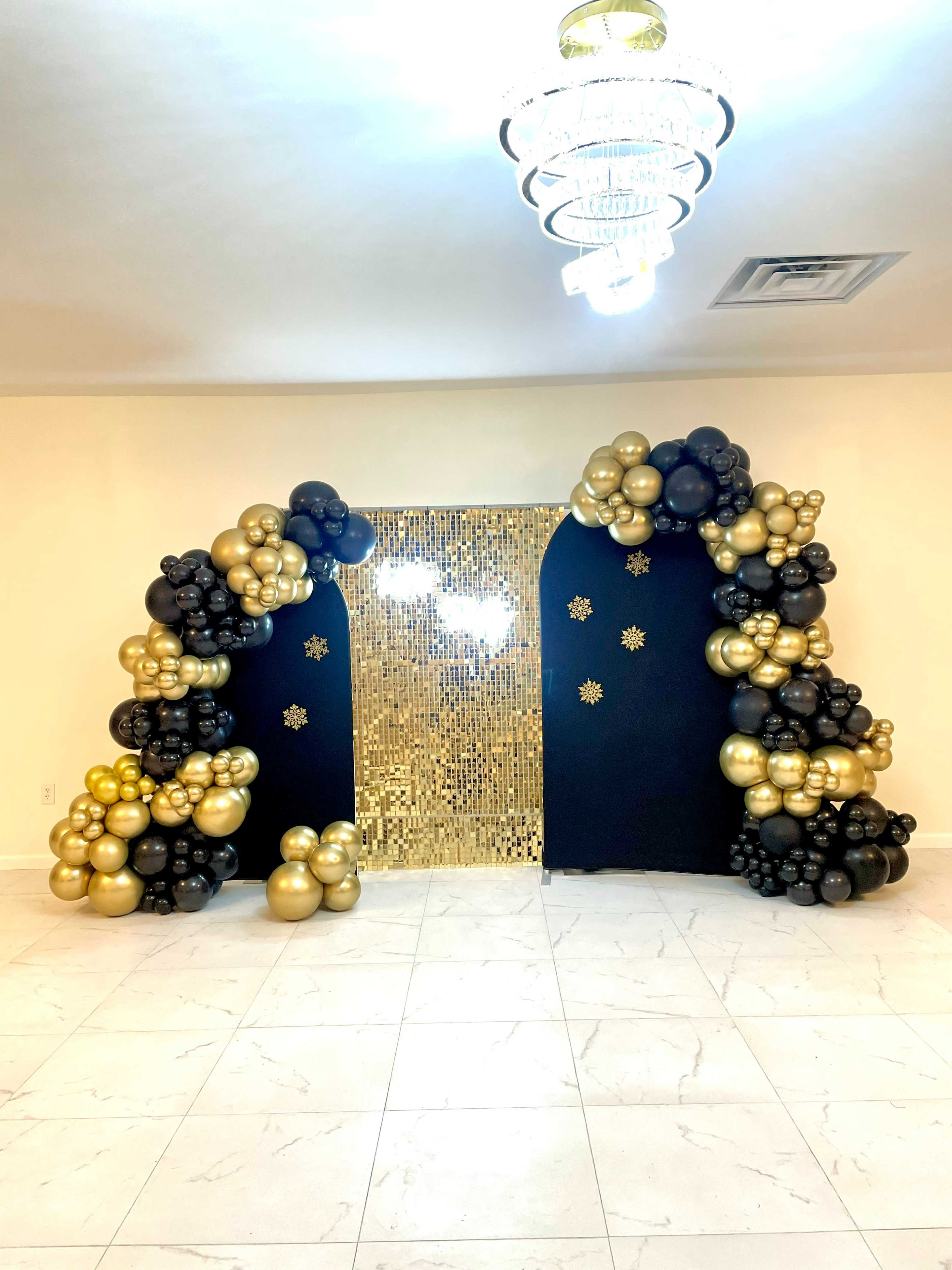 A backdrop decorated with clusters of black and gold balloons, flanking a shiny, sequined wall.