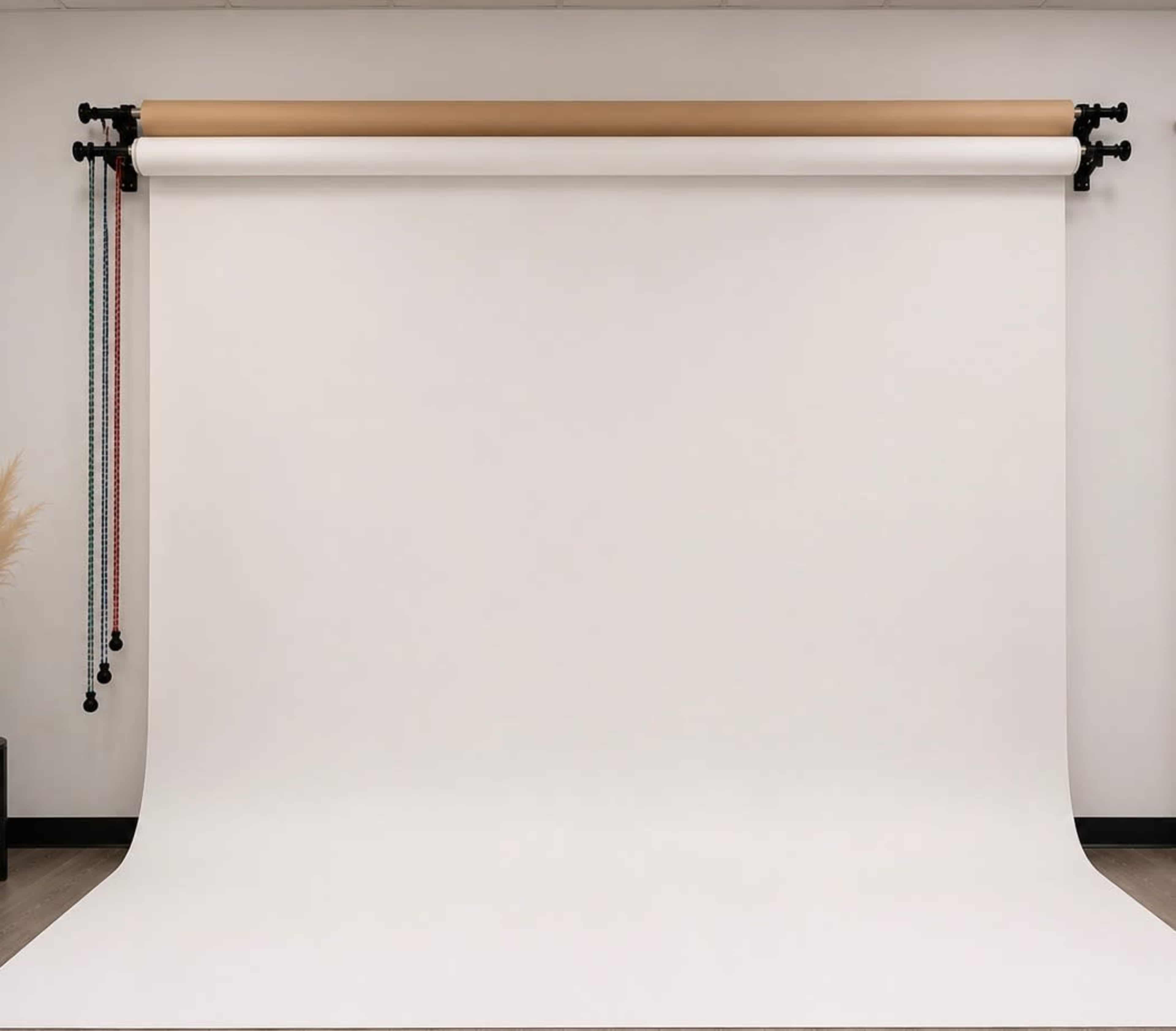 The image shows a blank studio backdrop with a white paper roll suspended from a black mounting system against a plain wall.