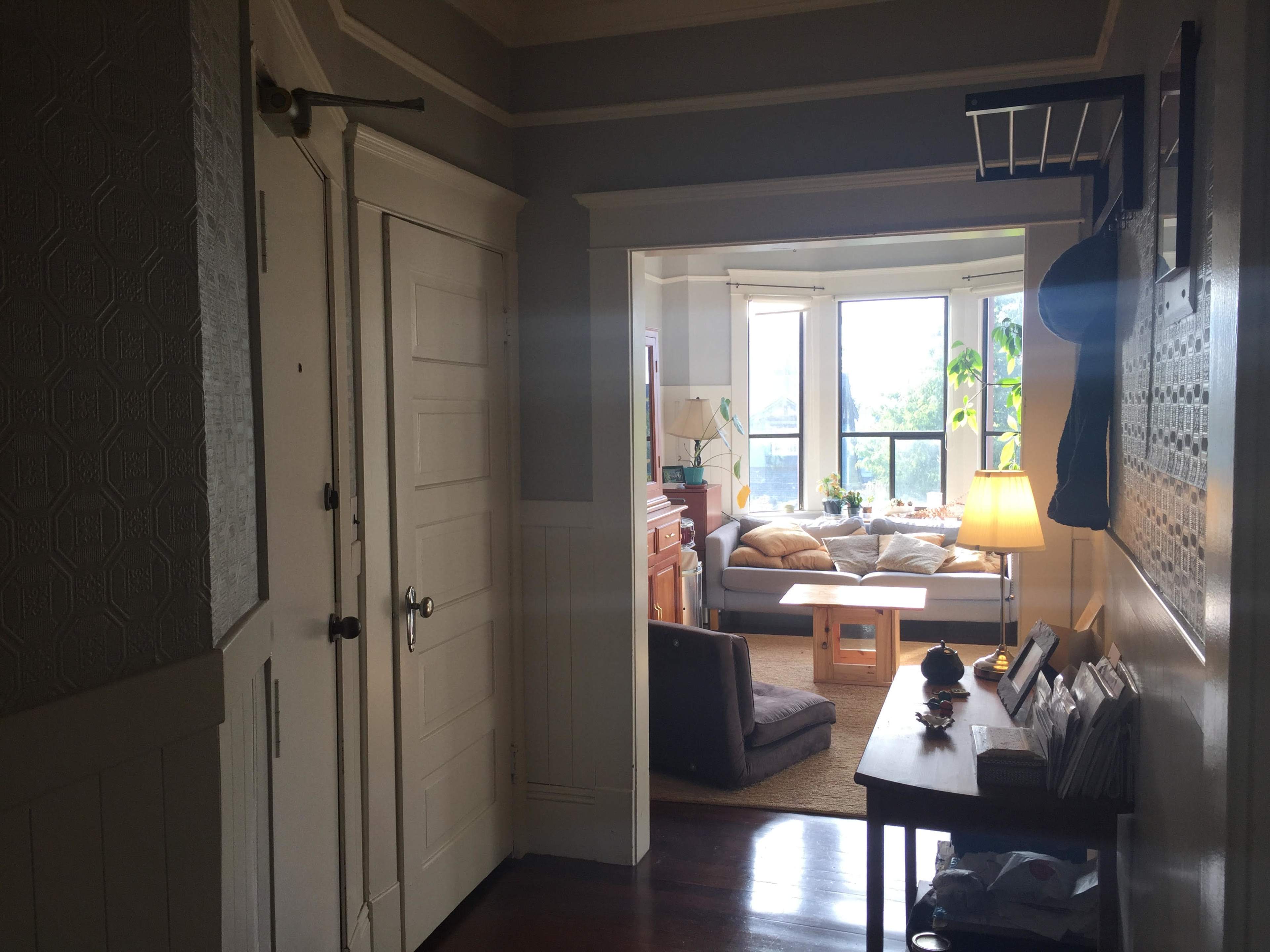 A hallway leads to a bright living room with large windows and cozy seating arrangements.