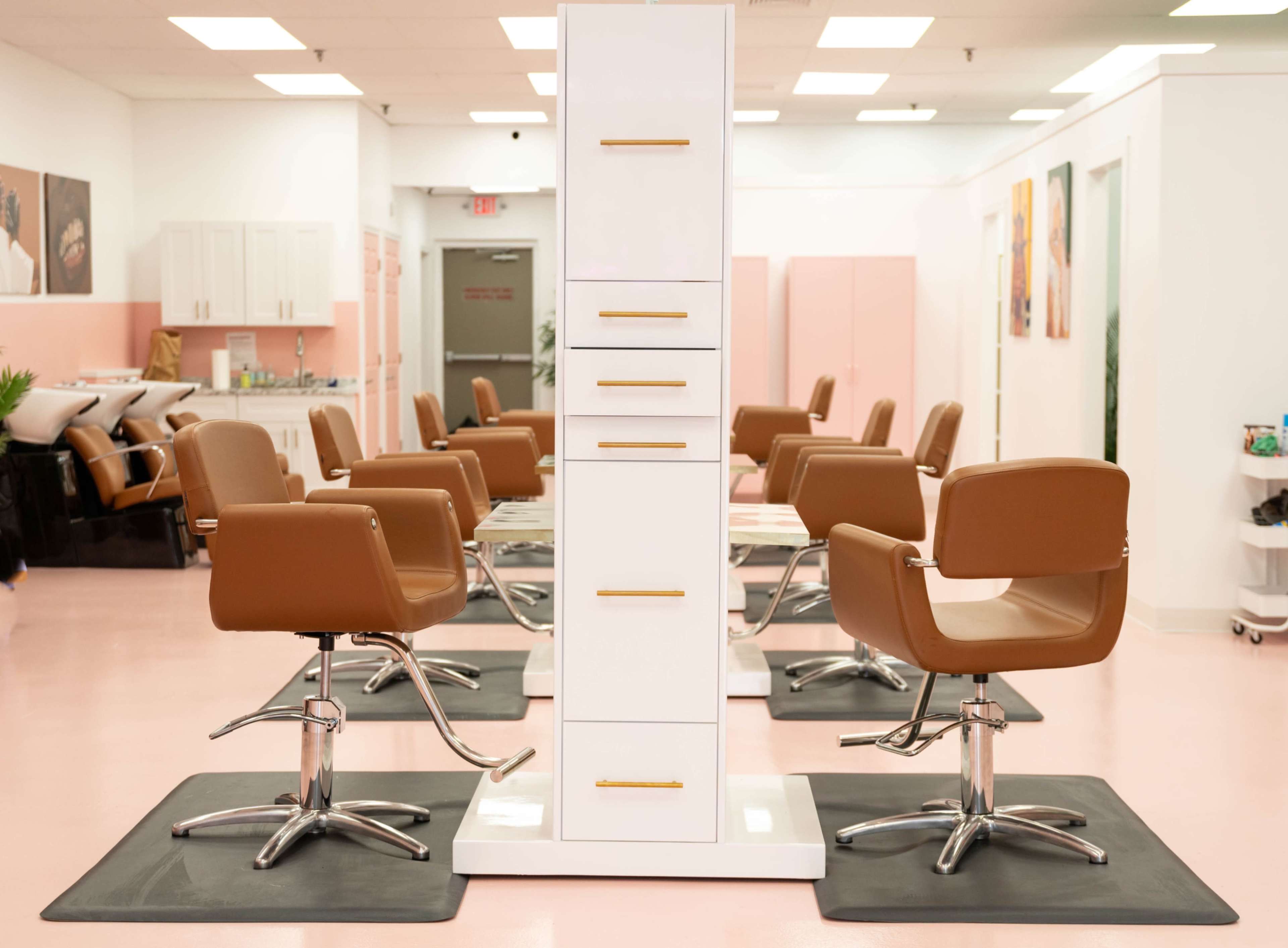 A modern hair salon with several styling chairs arranged around a central storage unit.
