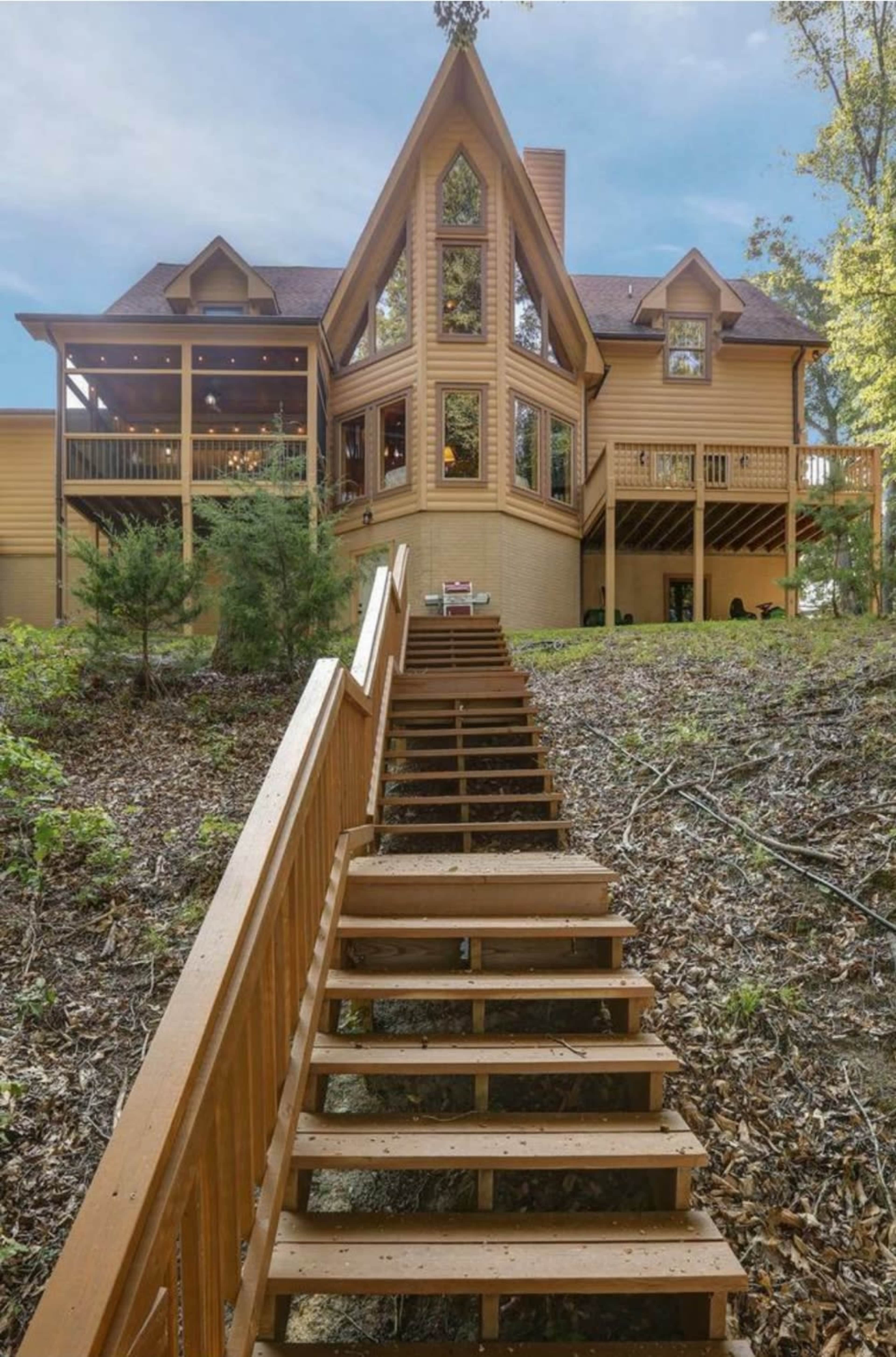 A large wooden house with an A-frame design, situated on a hillside with a staircase leading up to it.