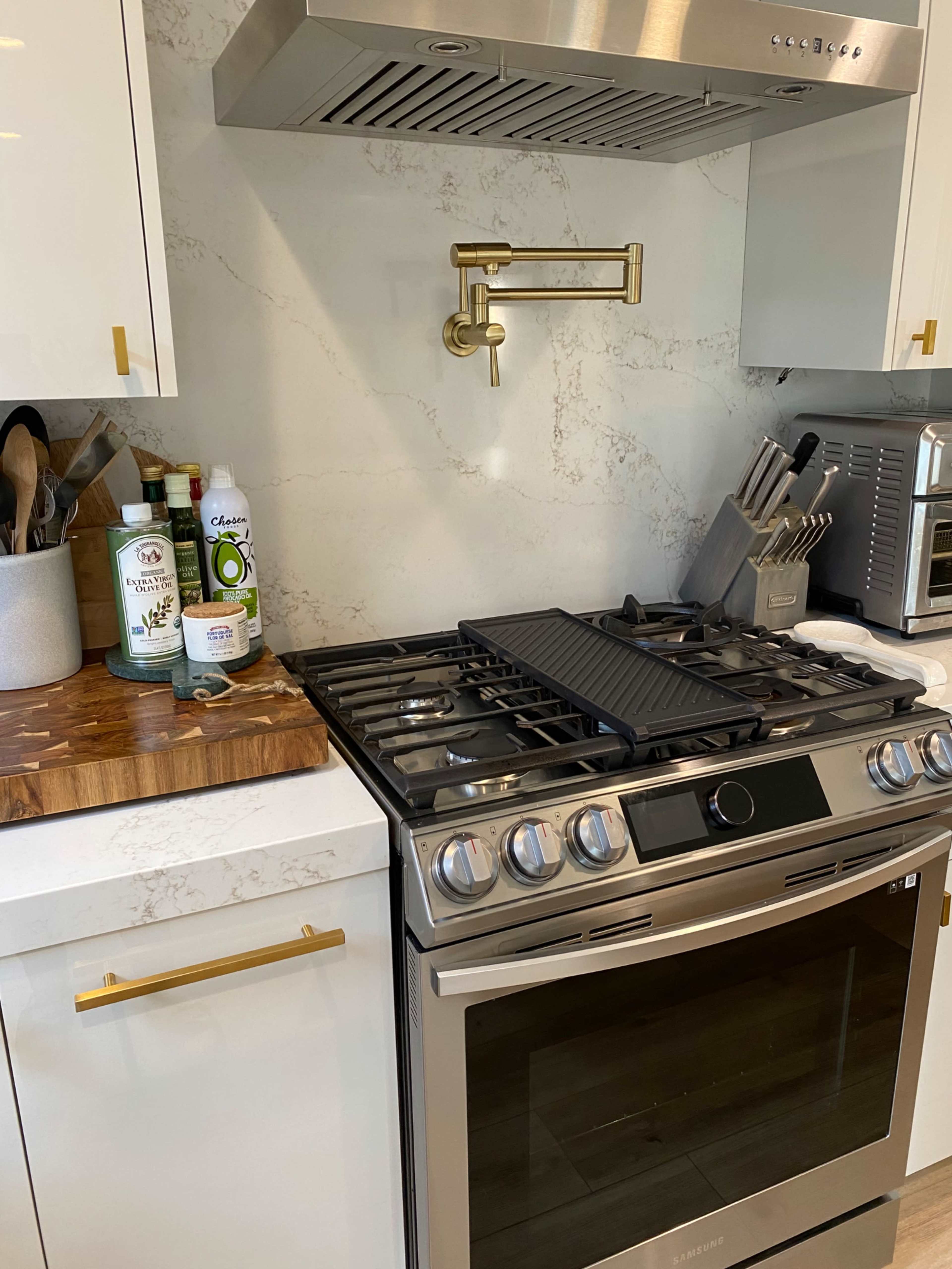 A modern kitchen with a stainless steel gas stove, a marble backsplash, and a wooden cutting board on the counter.