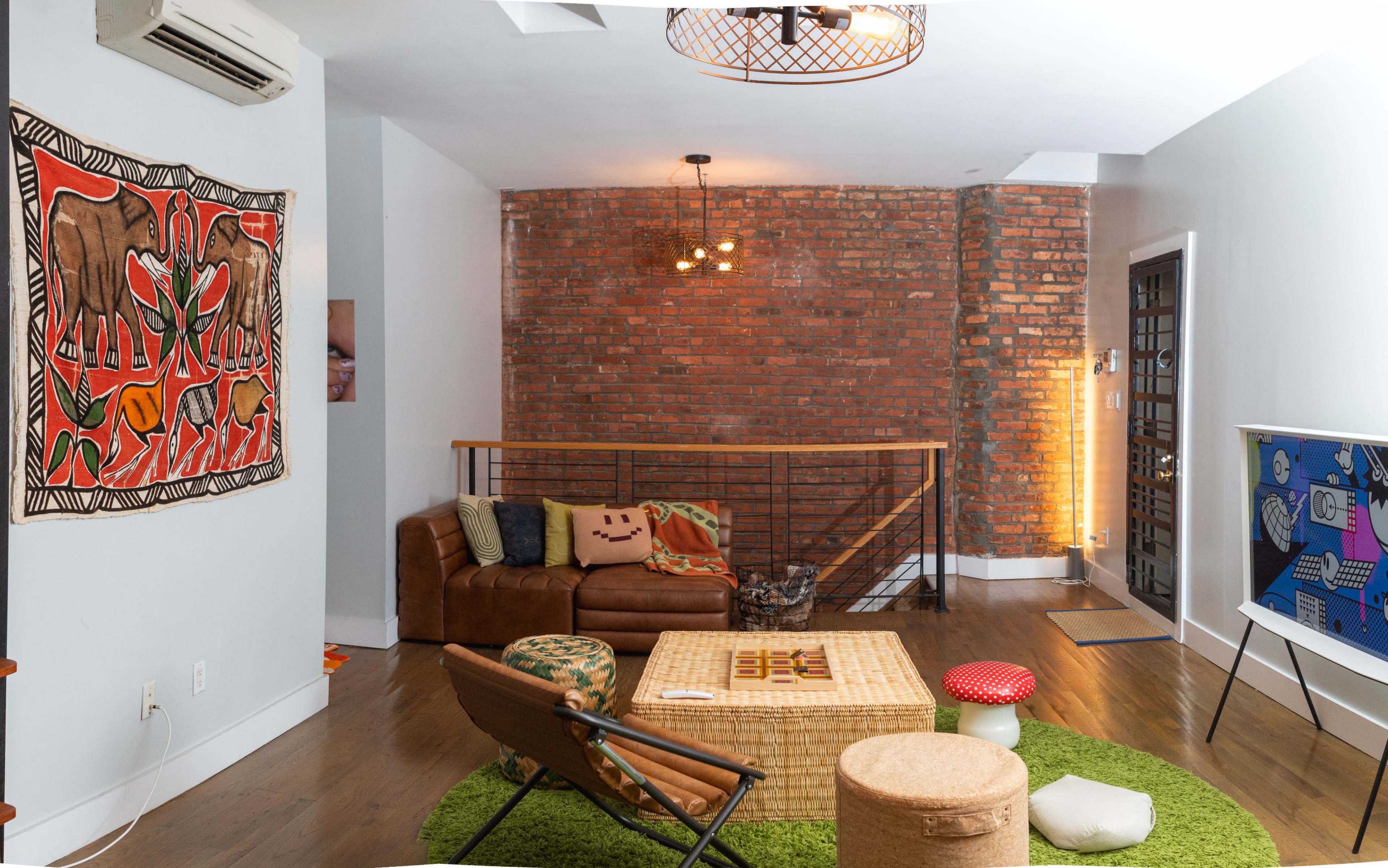 A modern living room with a brown leather sofa, a round green rug, and a large brick wall, complemented by a unique wall art piece and a contemporary light fixture.