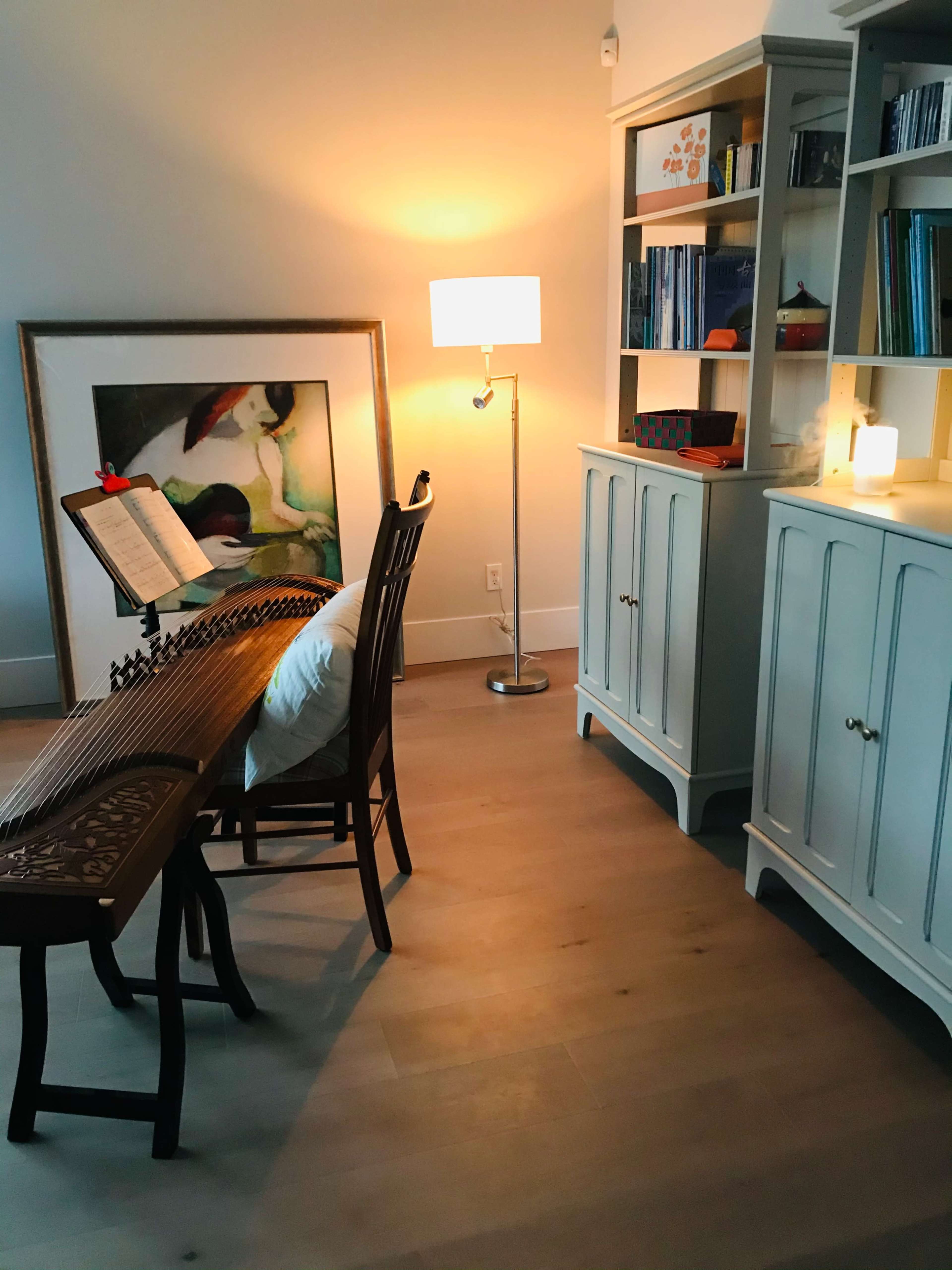 A chair and a music stand are positioned next to a lamp and a cabinet filled with books in a well-lit room.