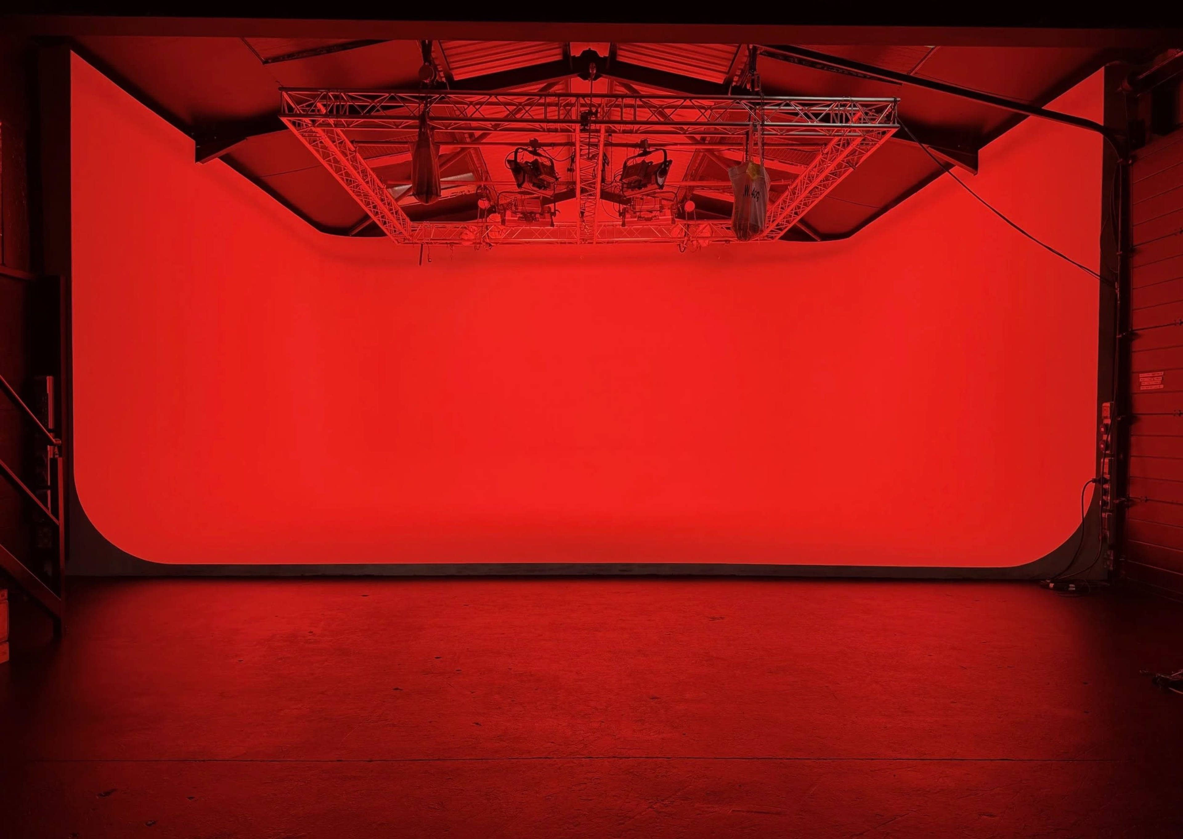 The image shows a spacious studio with a solid red backdrop and overhead lighting.