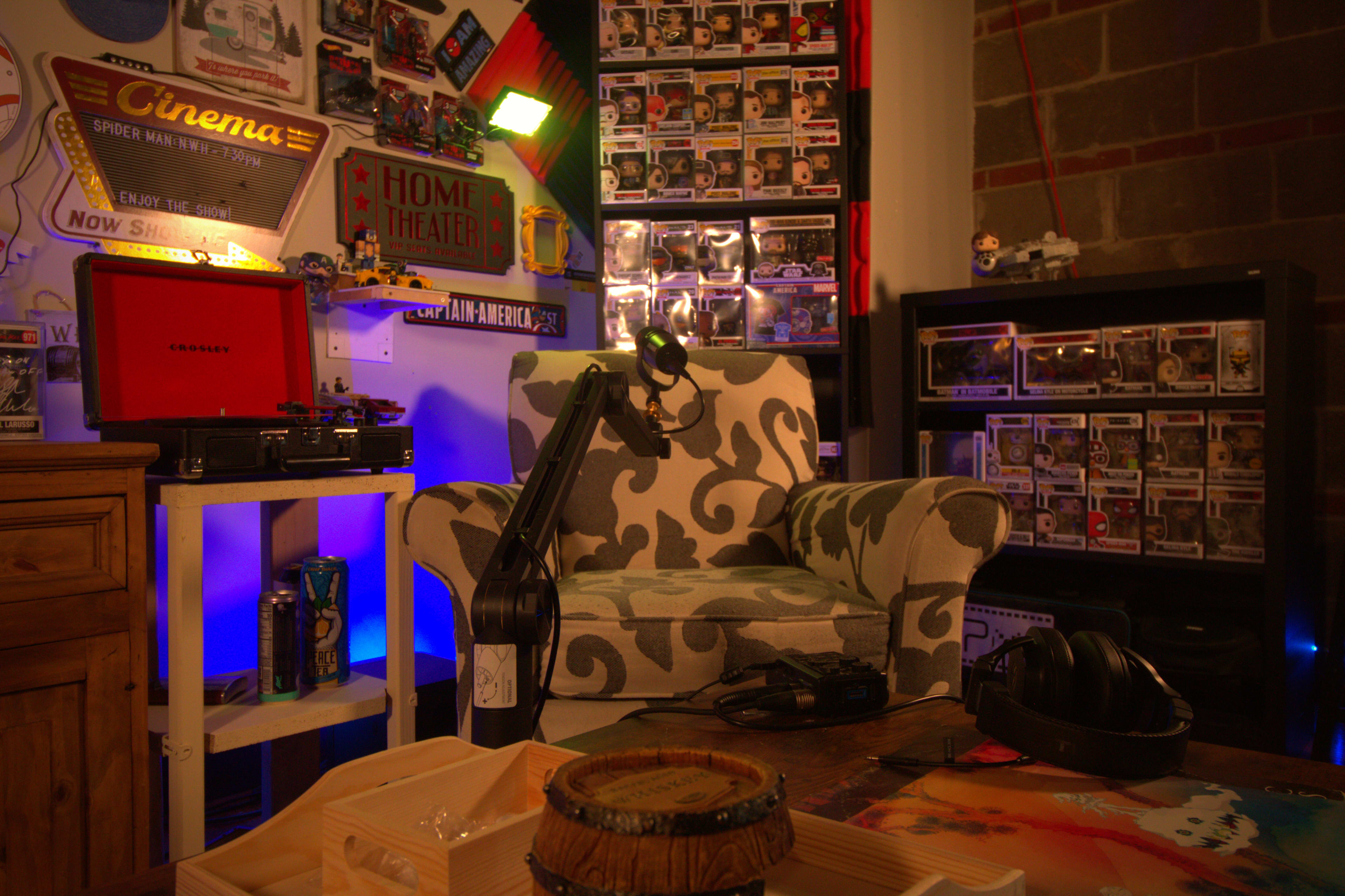 A cozy corner of a home theater displays a patterned armchair, a microphone on a stand, and shelves filled with collectible figurines.