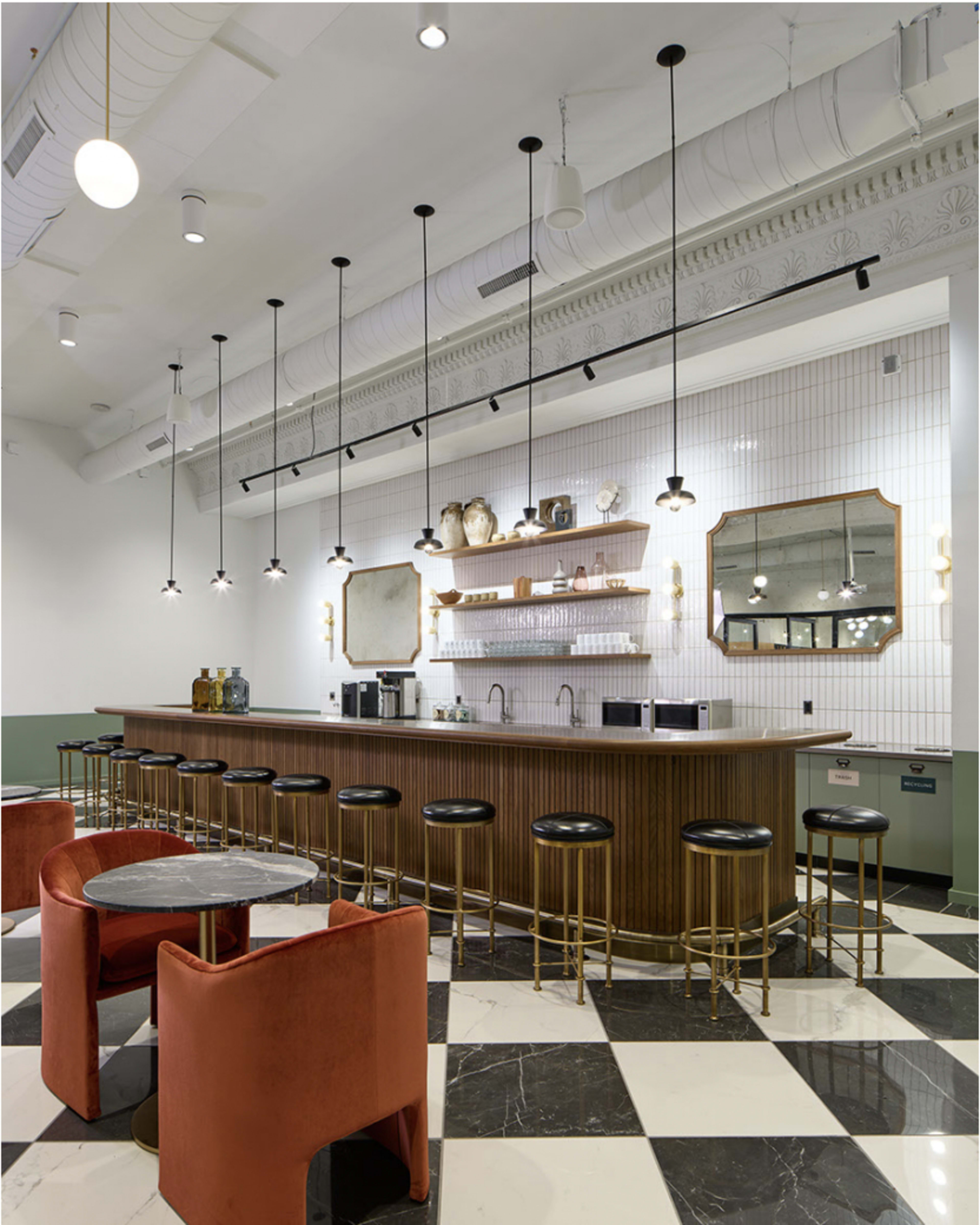 A modern café with a wooden bar, black stools, and pendant lights, featuring a patterned floor of black and white tiles.