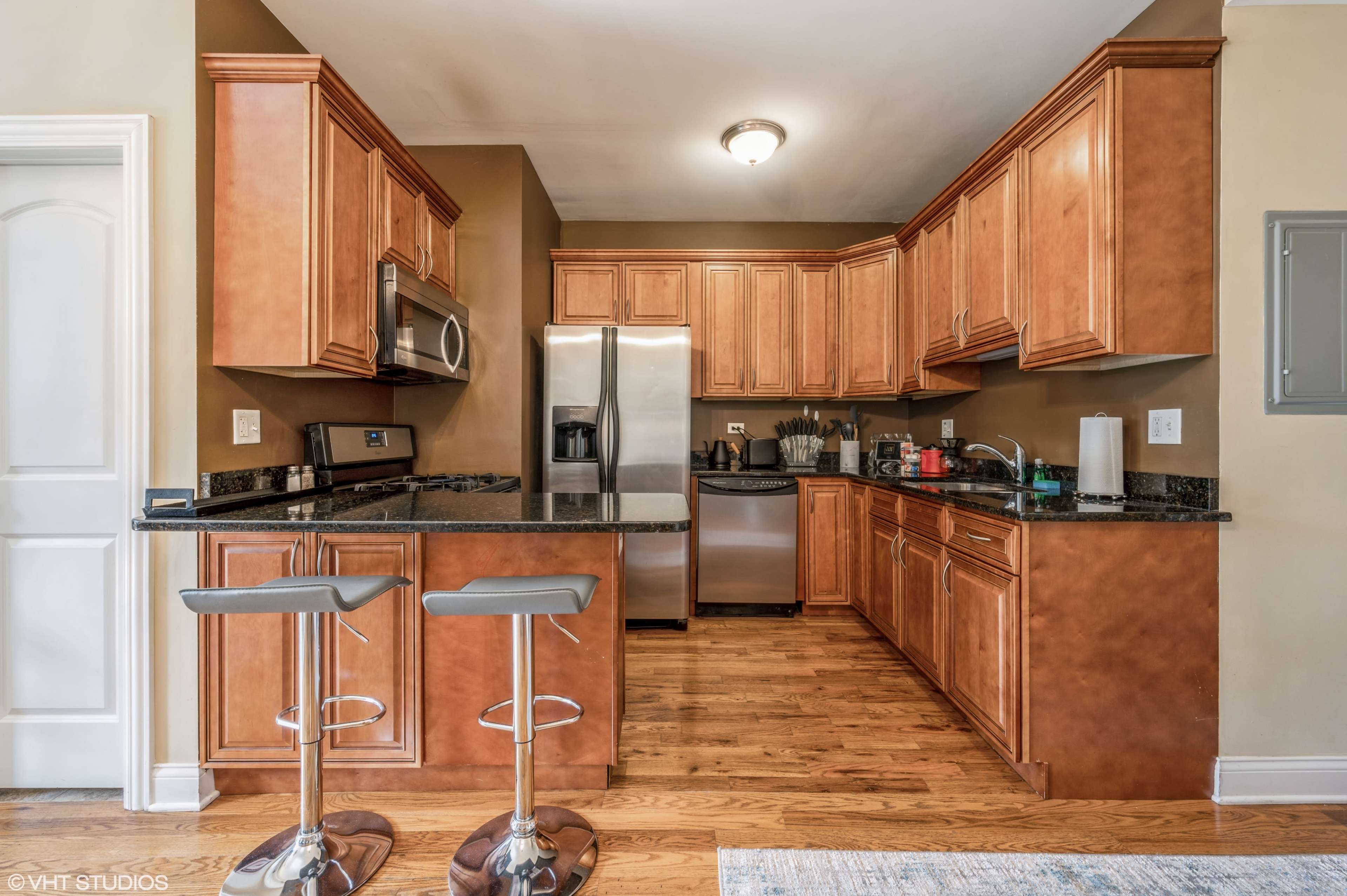 A kitchen featuring wooden cabinets, black granite countertops, stainless steel appliances, and barstool seating.