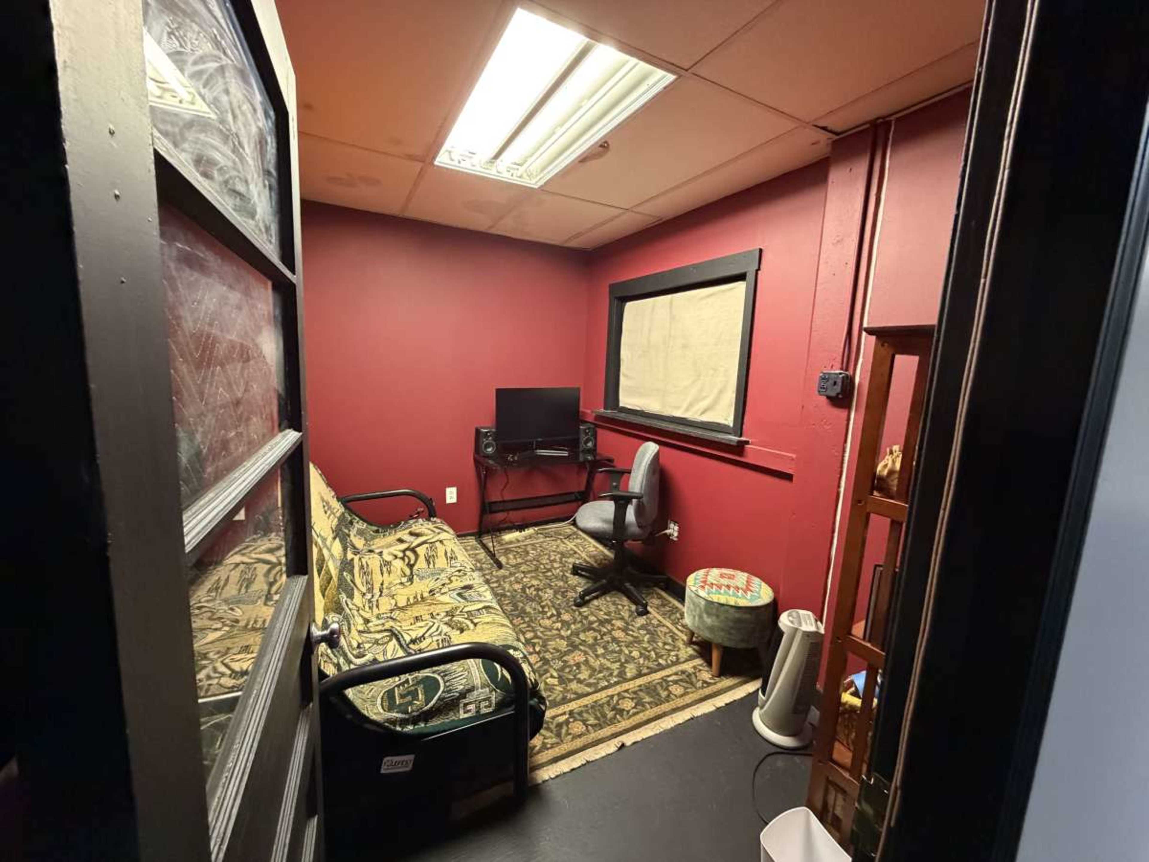 The image shows a small room with red walls, a patterned rug, a sofa, a desk chair, and a television on a stand.