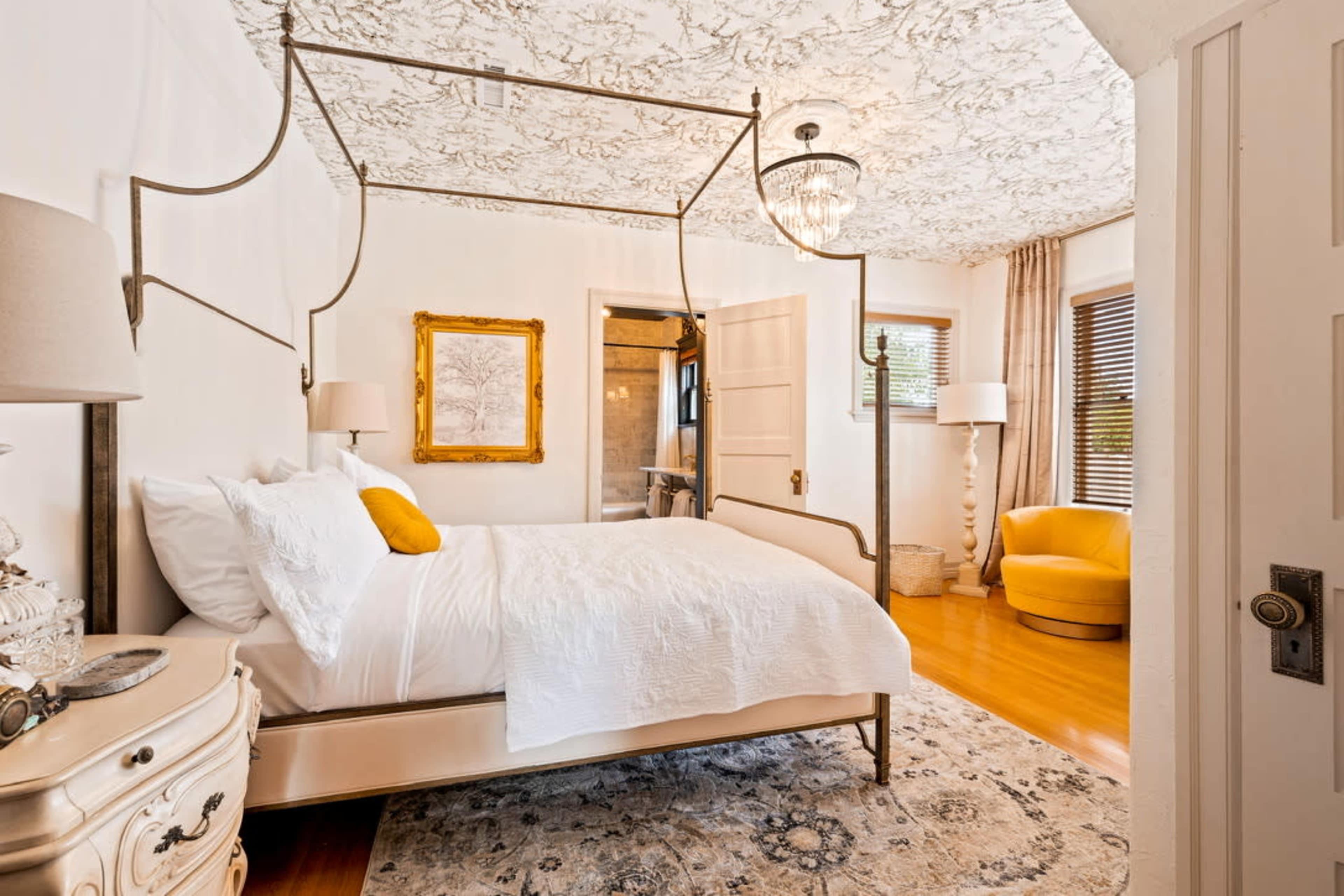 A bedroom featuring a four-poster bed, a vintage dresser, and a cozy seating area with a yellow chair.