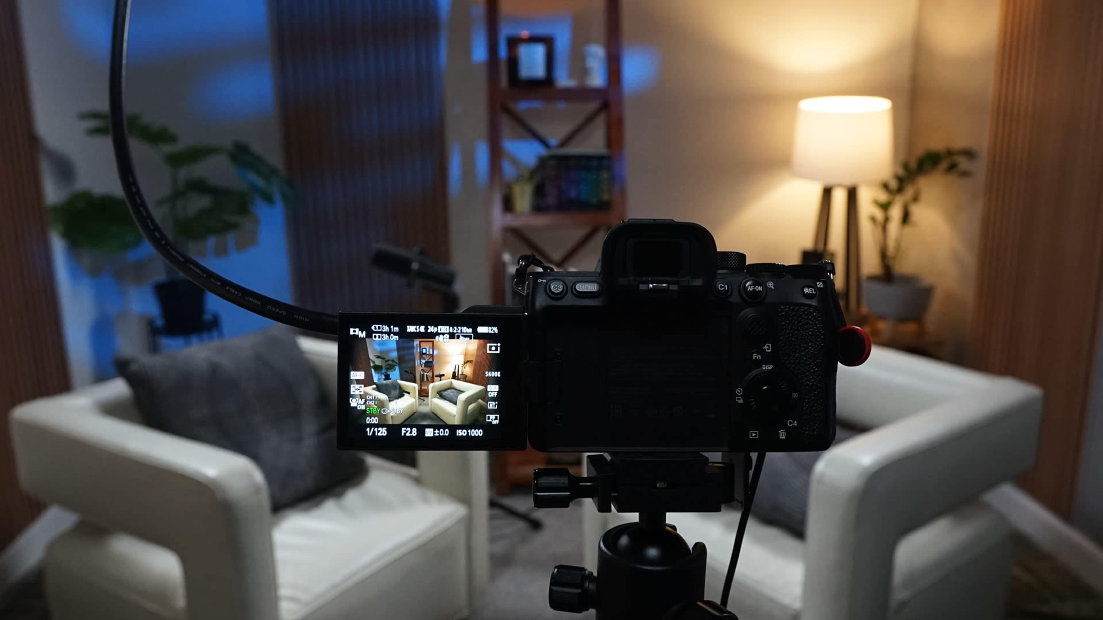 A camera on a tripod is focused on two white armchairs in a well-lit living room setting.