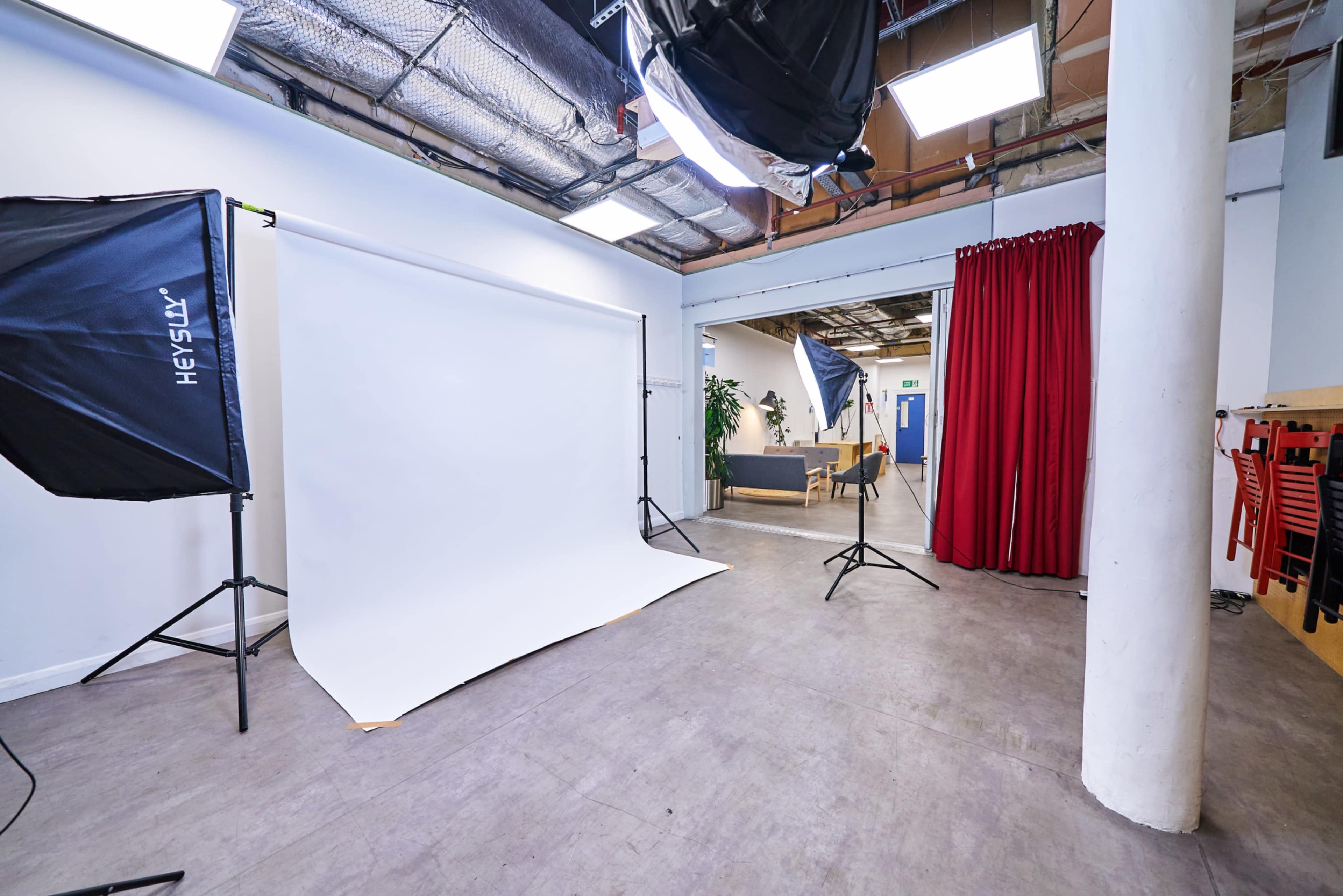 The image depicts a photography studio with a backdrop set up, lighting equipment, and a seating area in the background.