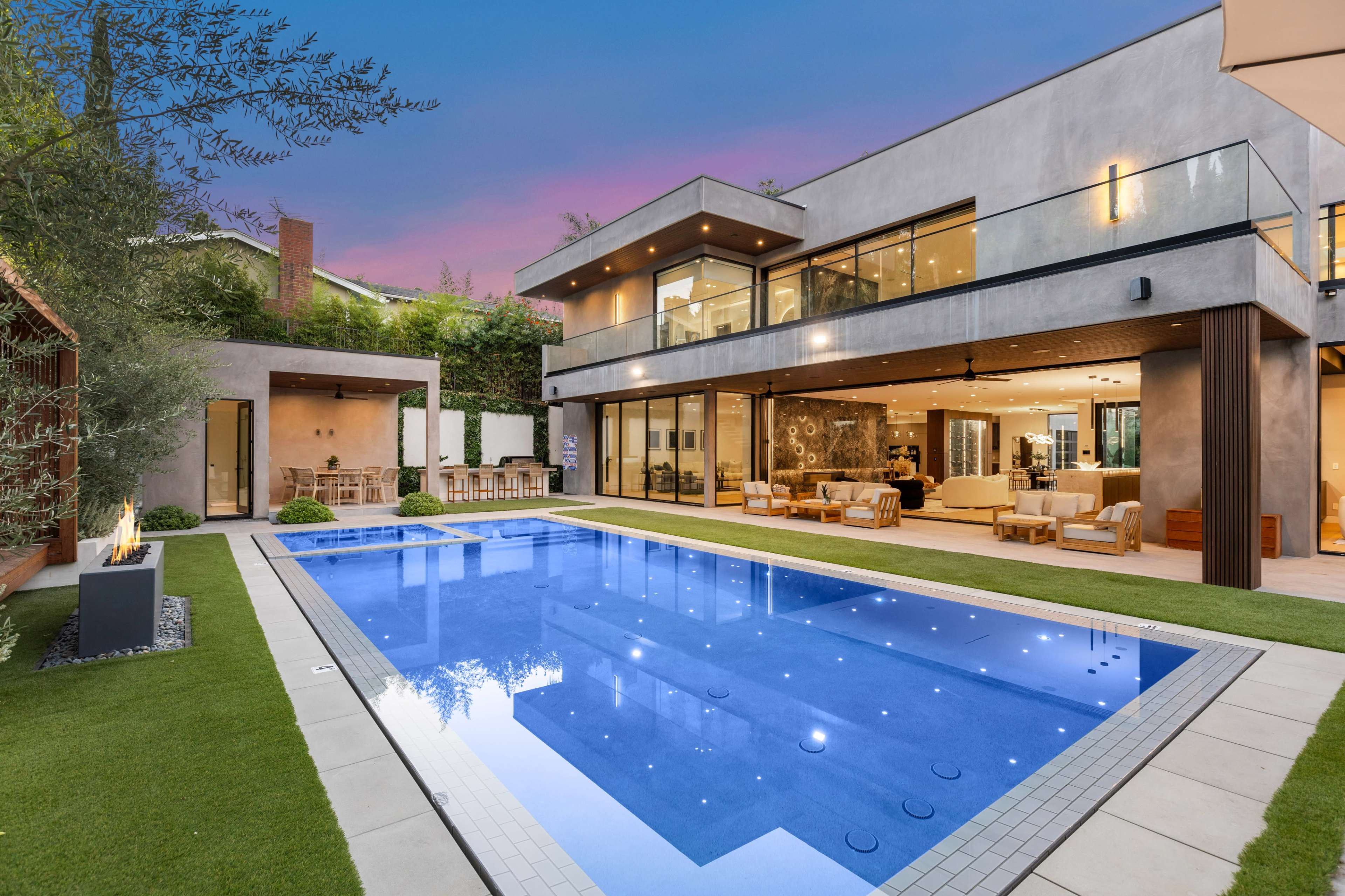 A modern house with a large swimming pool and outdoor seating area is set against a twilight sky.