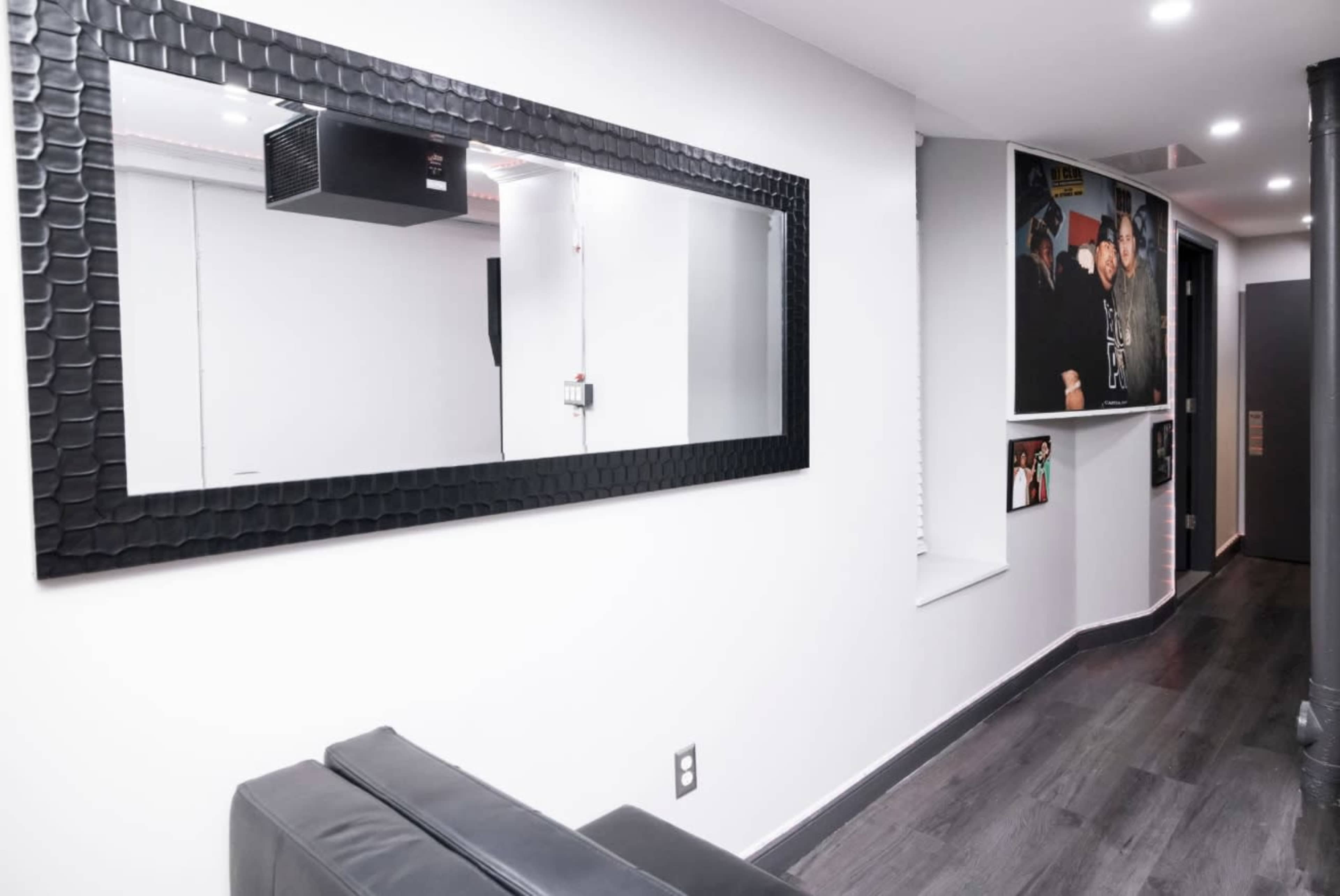The image shows a modern hallway with a black-framed mirror, seating area, and framed pictures on the walls.