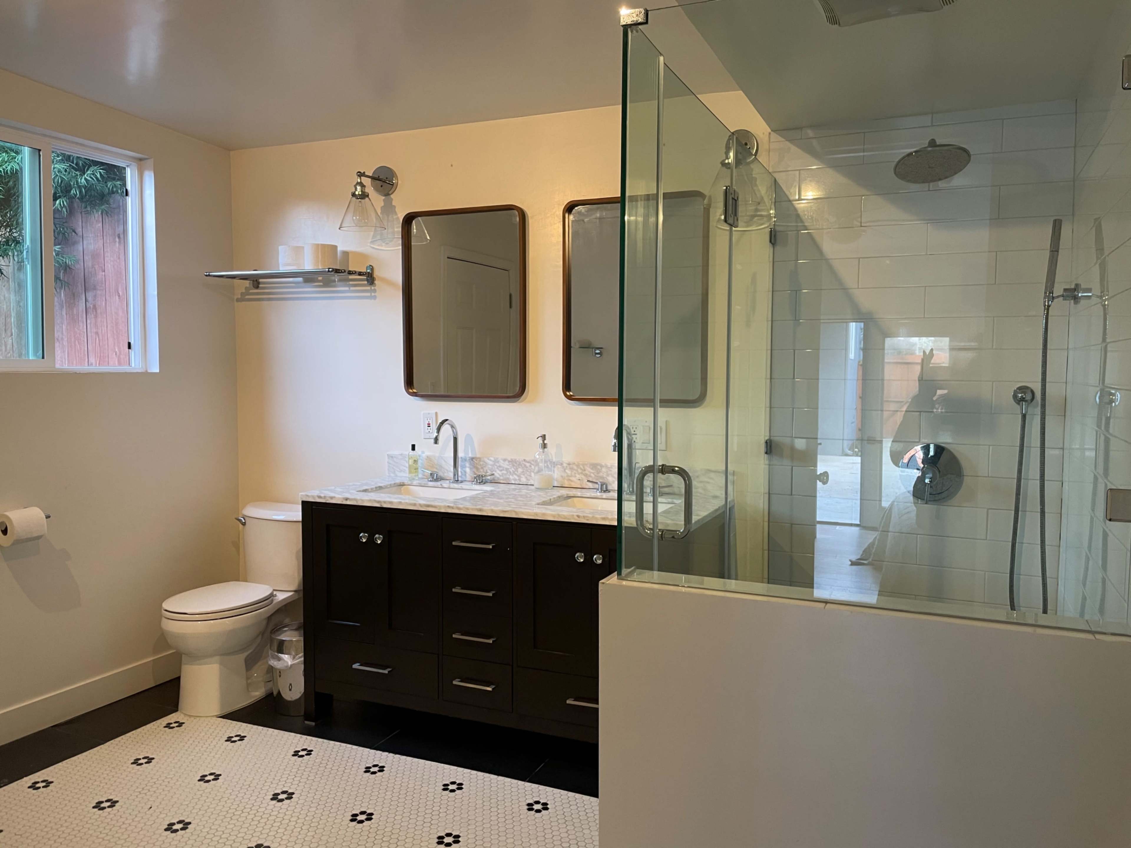 A modern bathroom featuring a glass shower, a dual-sink vanity with dark cabinetry, and a tiled floor with a floral pattern.