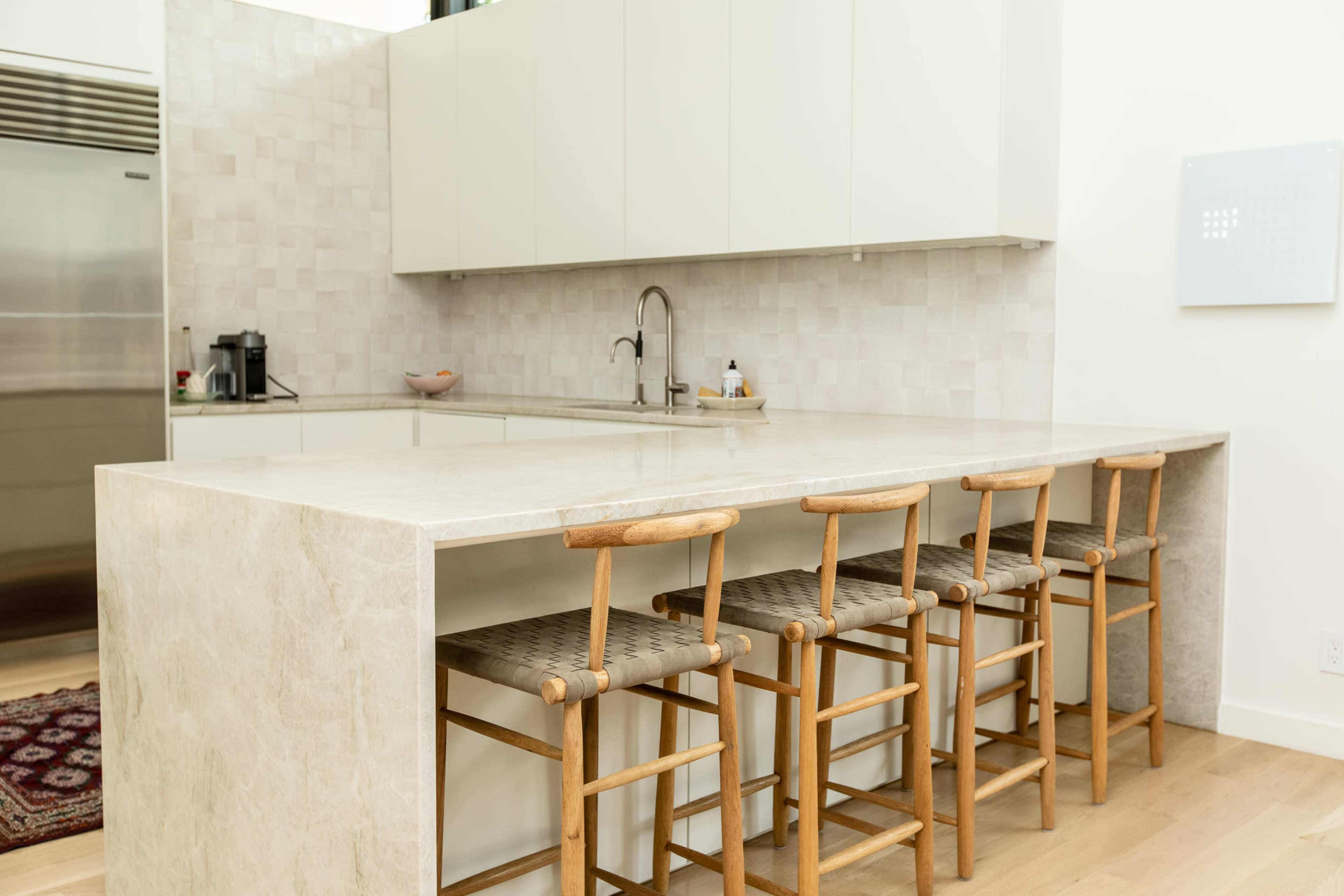 A modern kitchen with a large stone countertop and four wooden stools arranged around it.