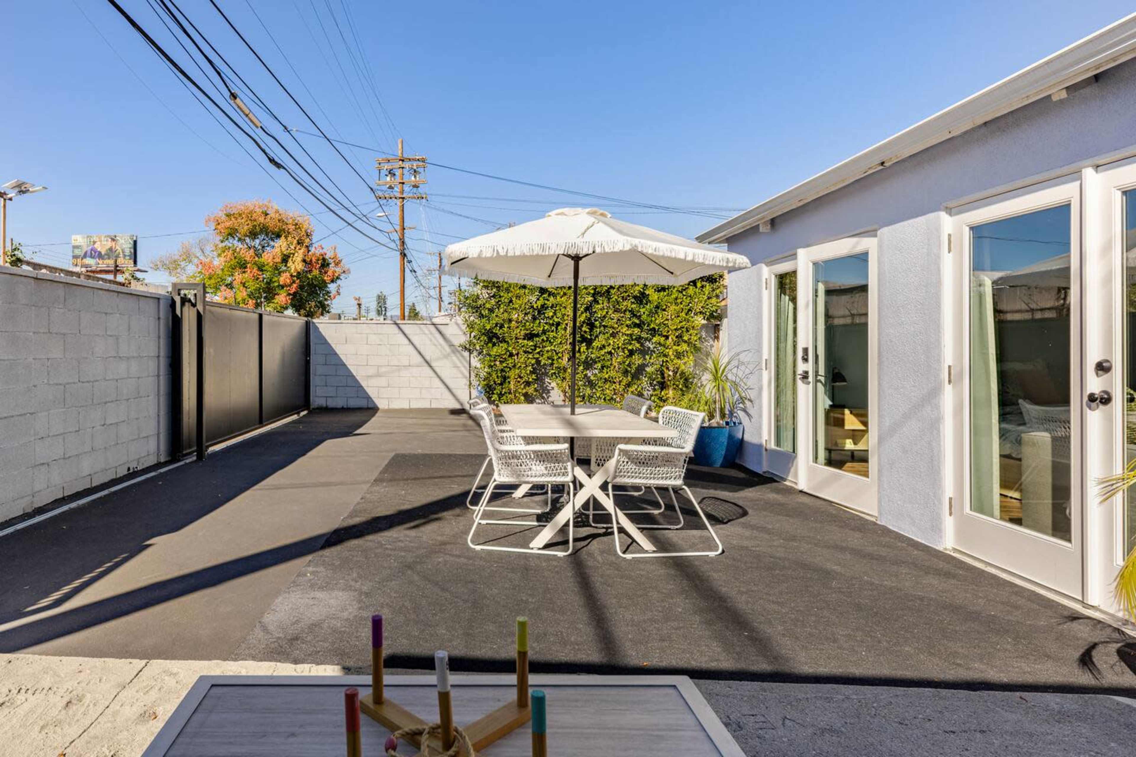 A patio area features a table and chairs beneath a large umbrella, surrounded by a concrete wall and clear blue sky.
