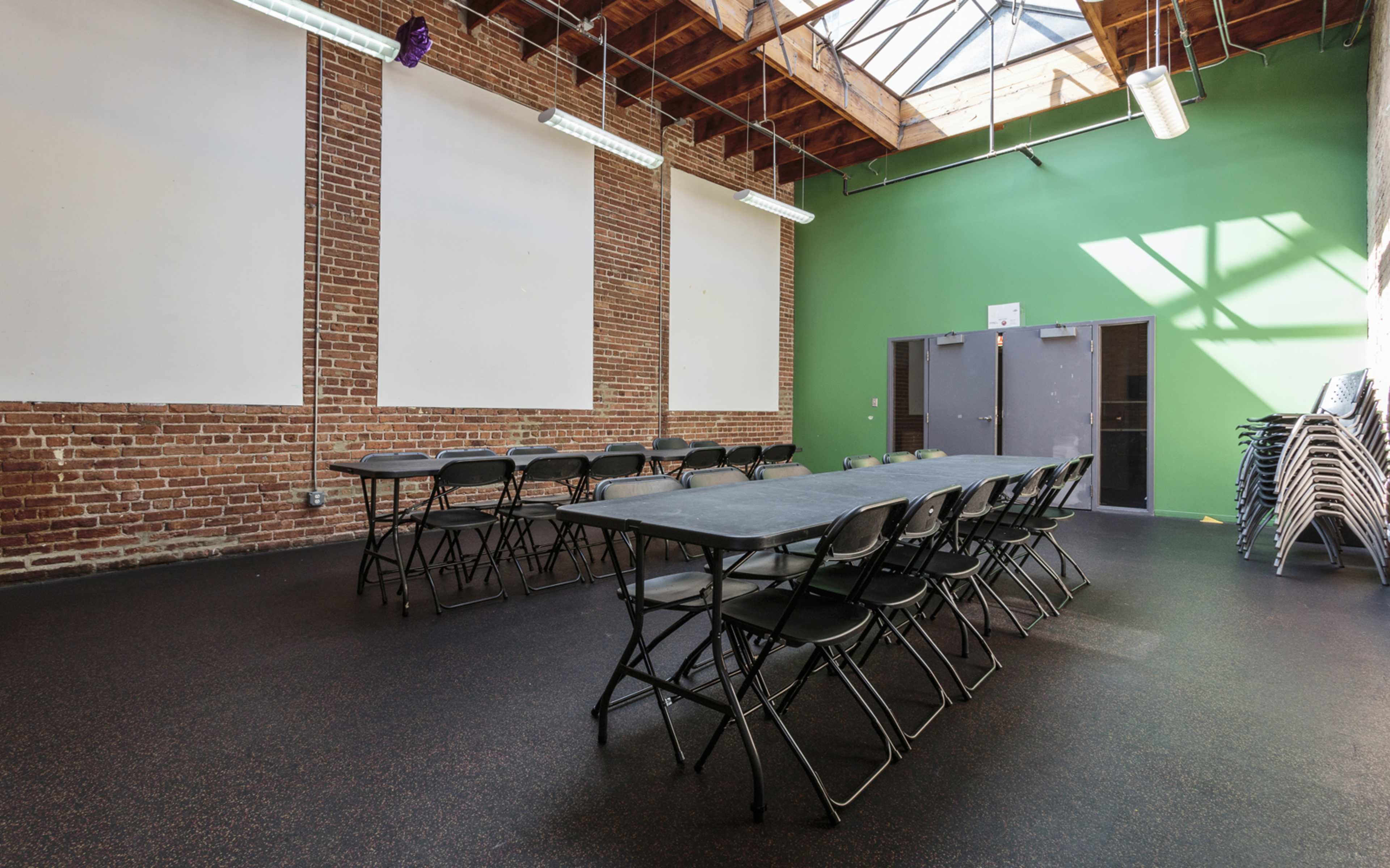 A spacious room with a black floor, green walls, and two long tables set up in a U-shape under a skylight.