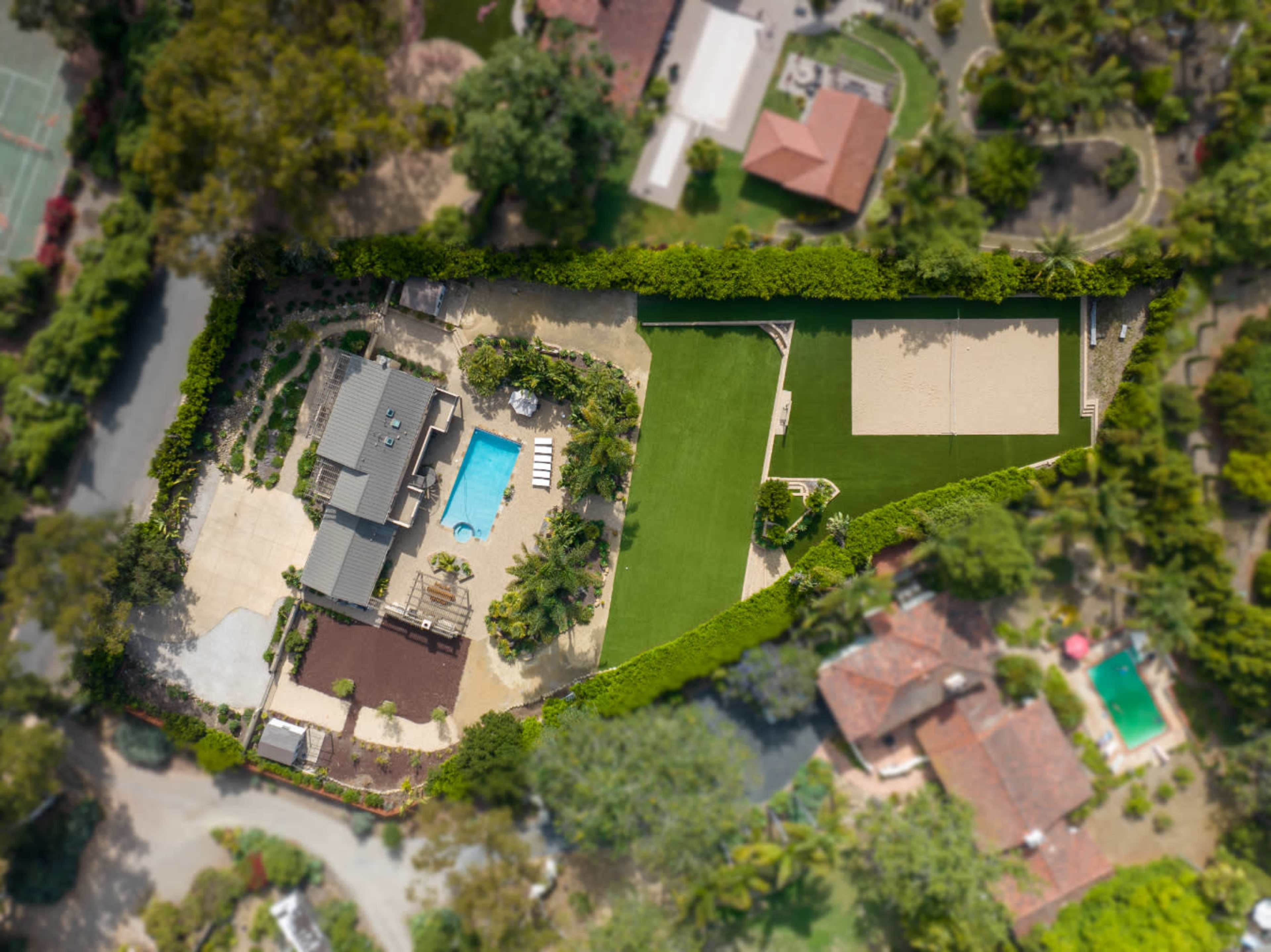 An aerial view of a residential property featuring a house, pool, landscaped areas, and a tennis court.