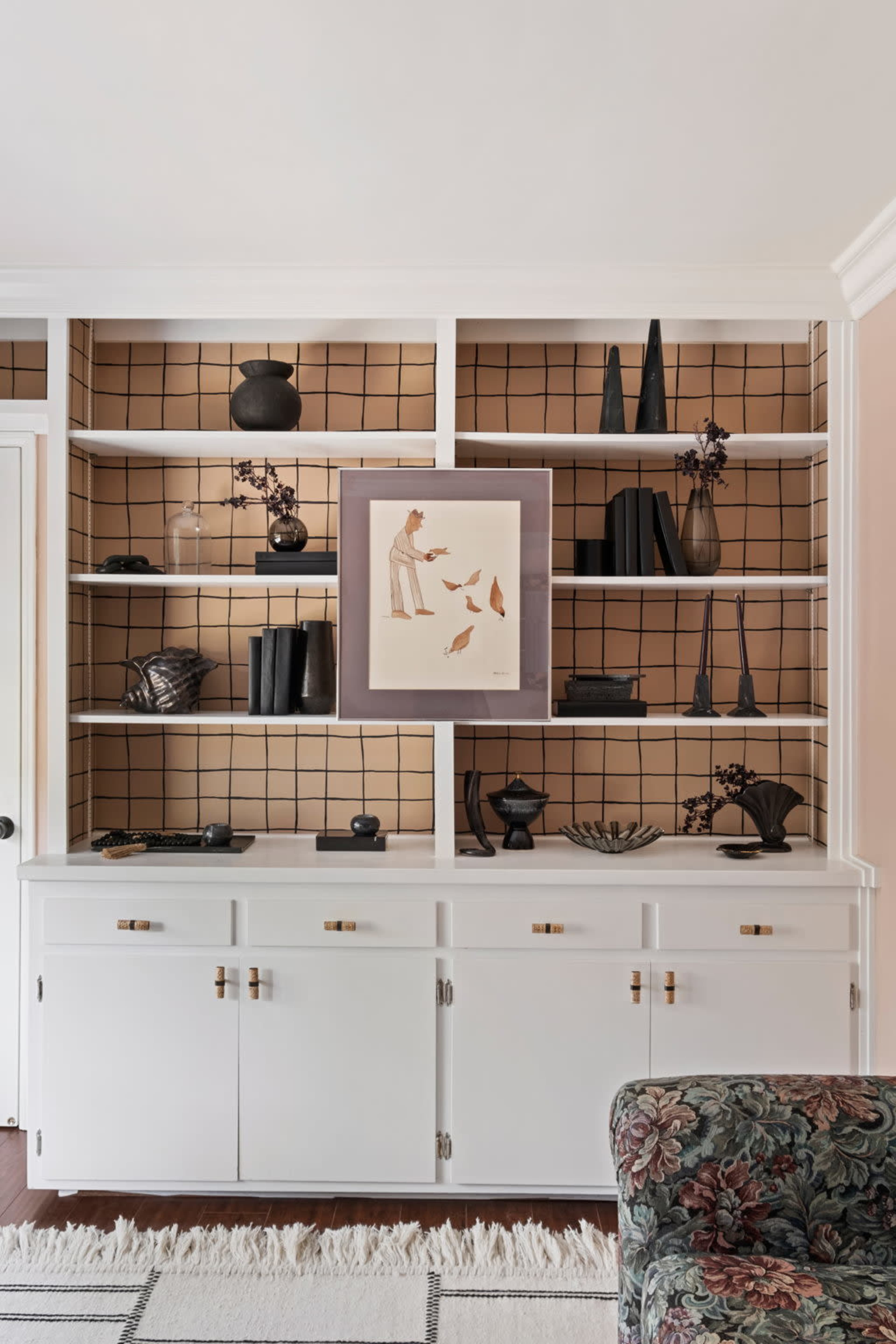 A white shelving unit with a grid-patterned backdrop, displaying various black decorative items and a framed artwork.
