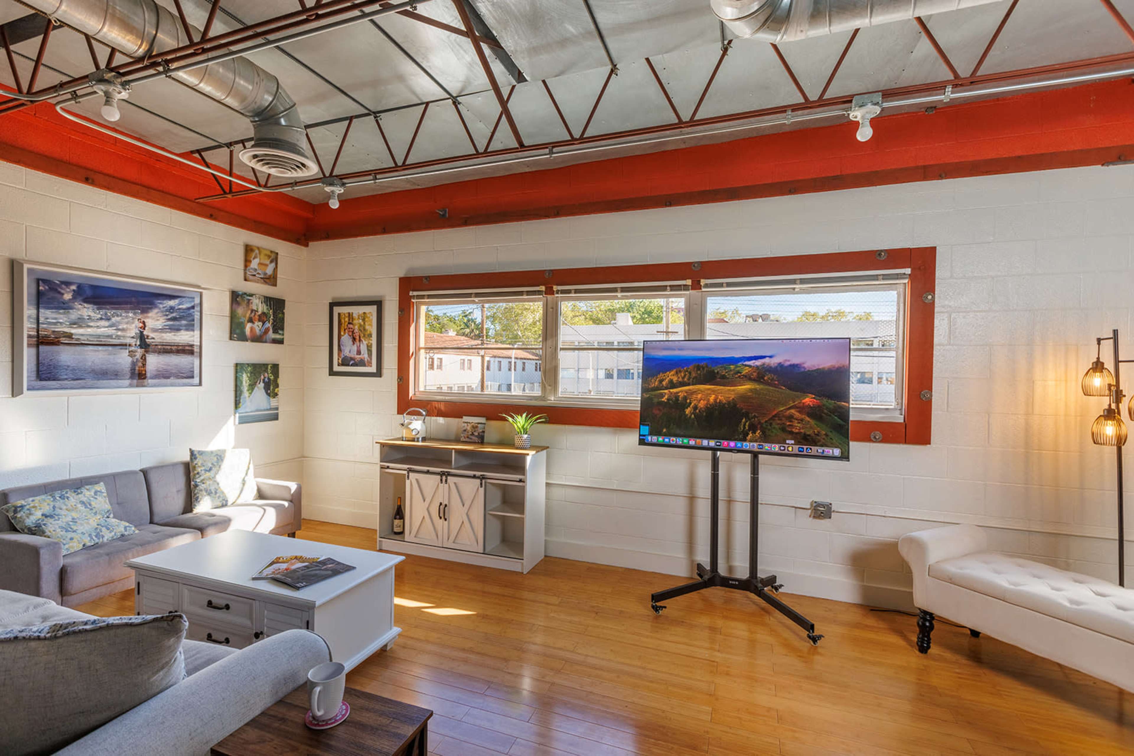 A bright living room with large windows, a comfortable seating area, and a television mounted on a stand.