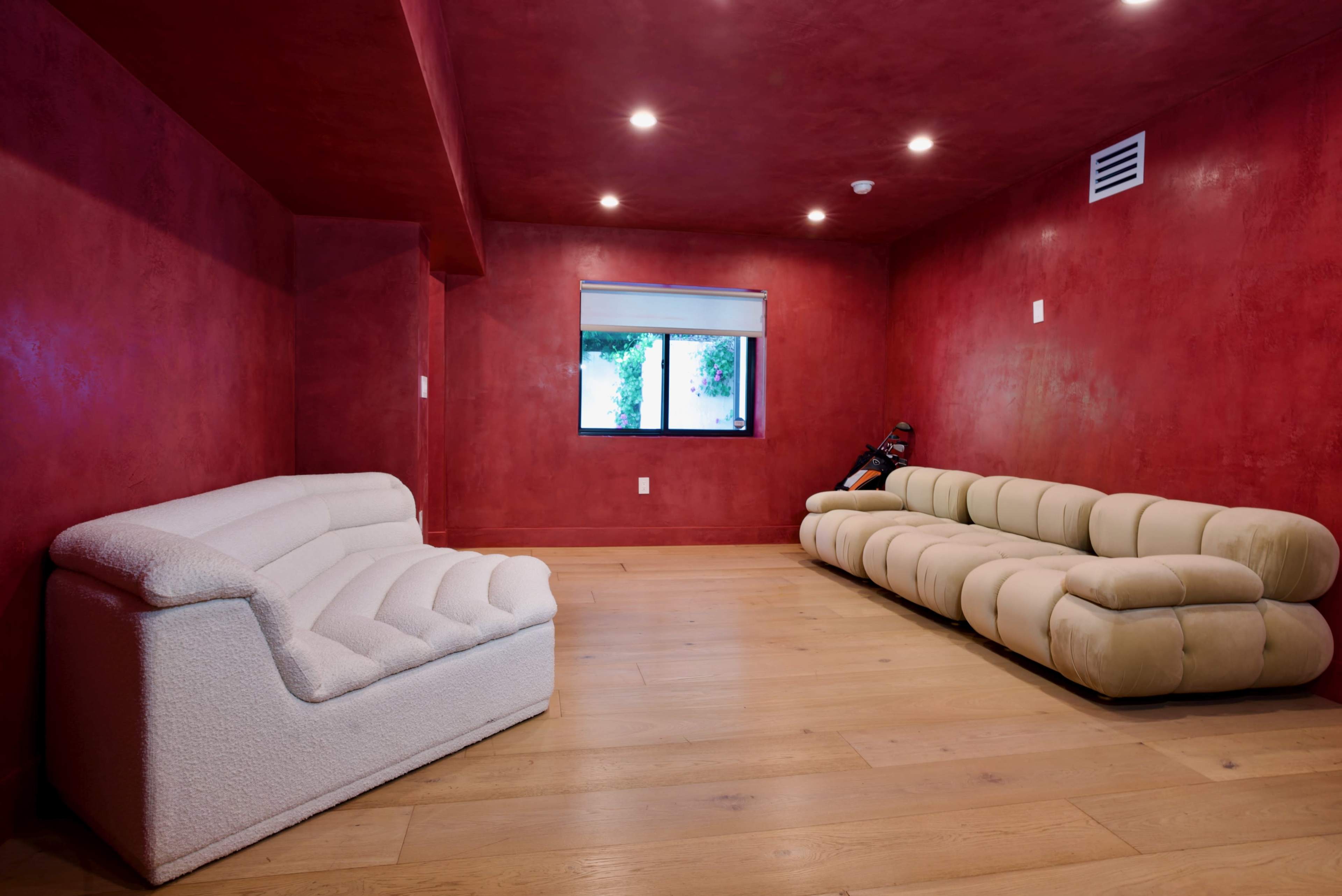 The image shows a room with red walls, a light-colored floor, and two sofas arranged with one near the window.