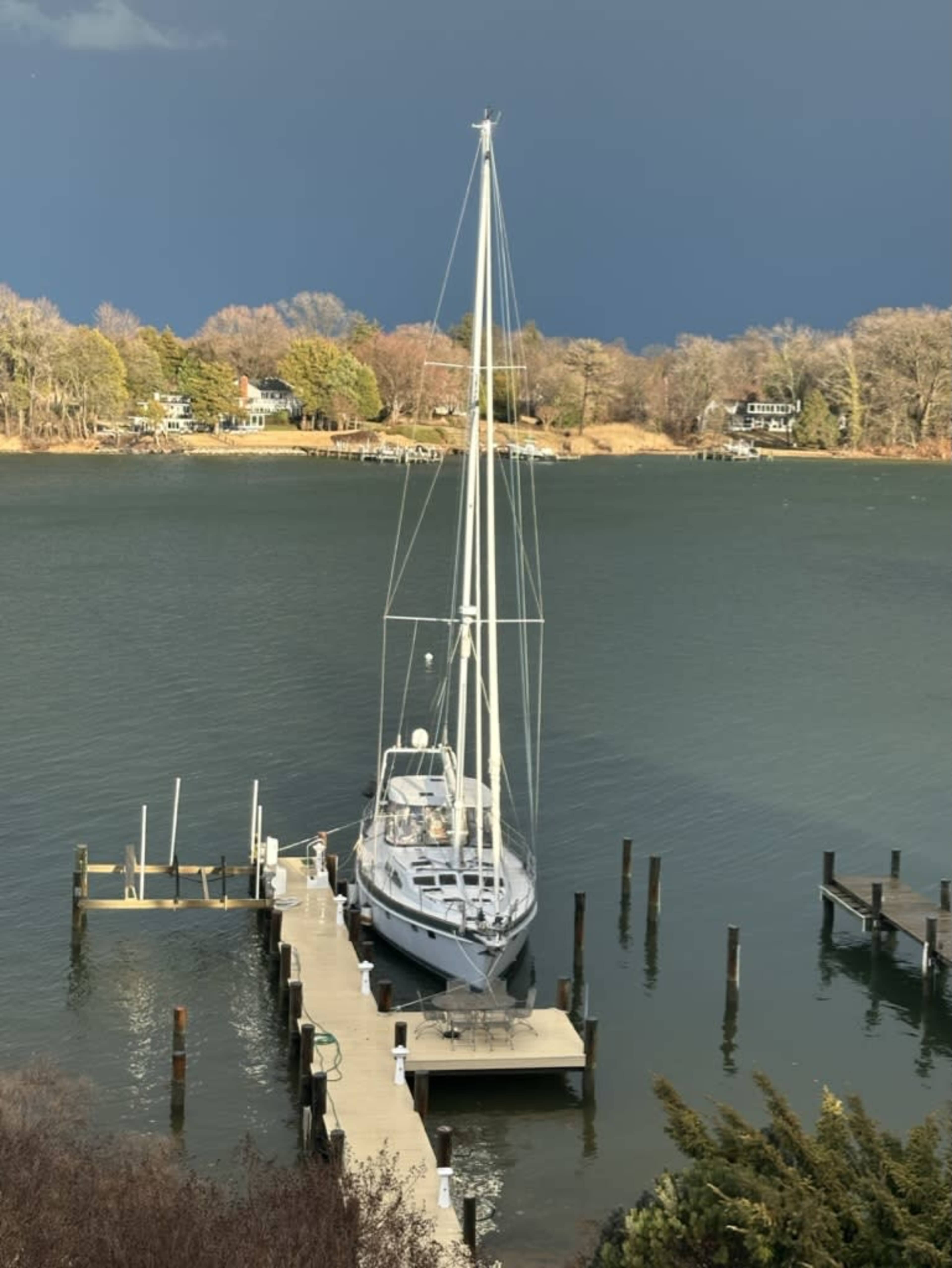 A sailboat is docked at a pier on a calm body of water, with dark storm clouds looming in the background.