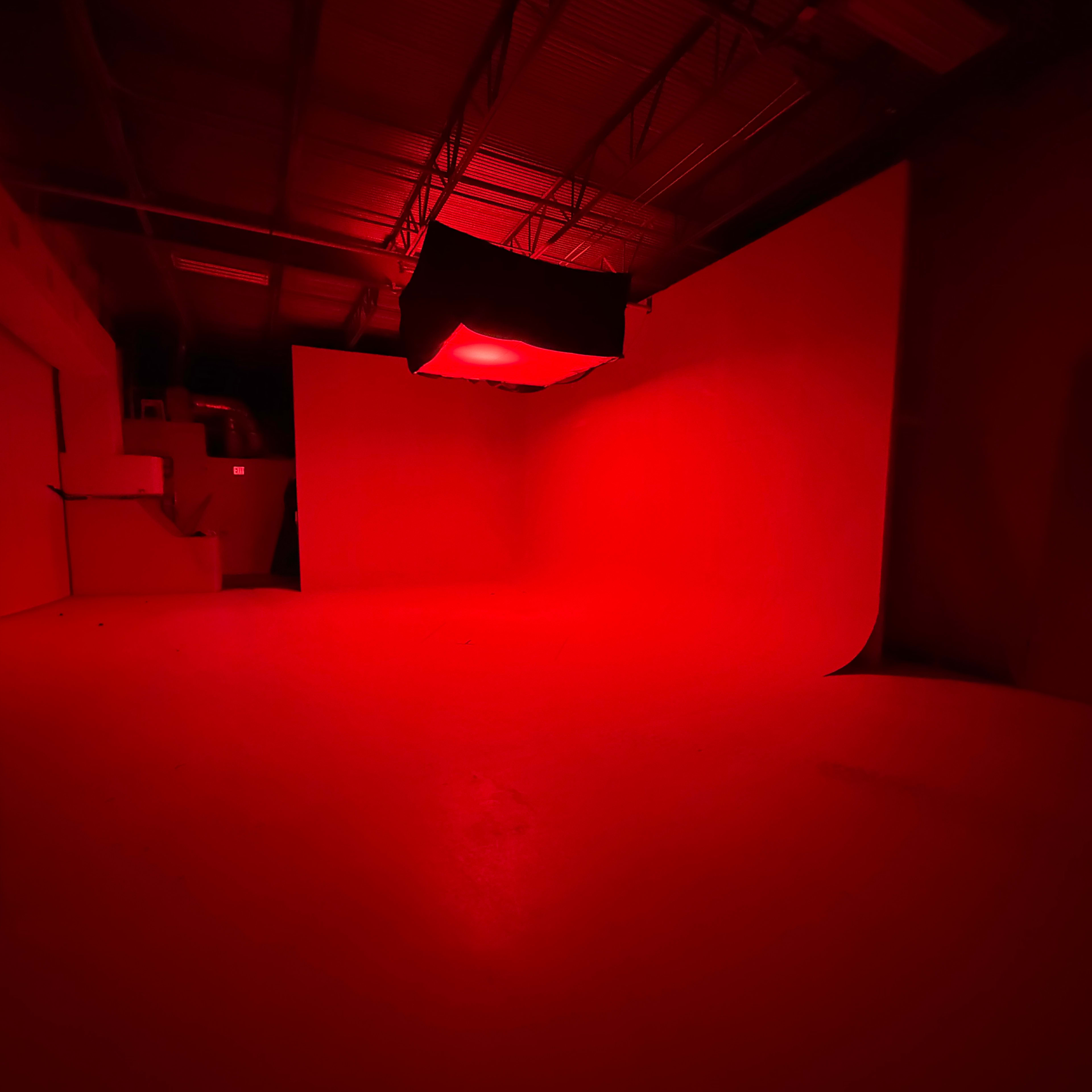 The image shows a studio space illuminated in red light, featuring a curved backdrop and a suspended light fixture.